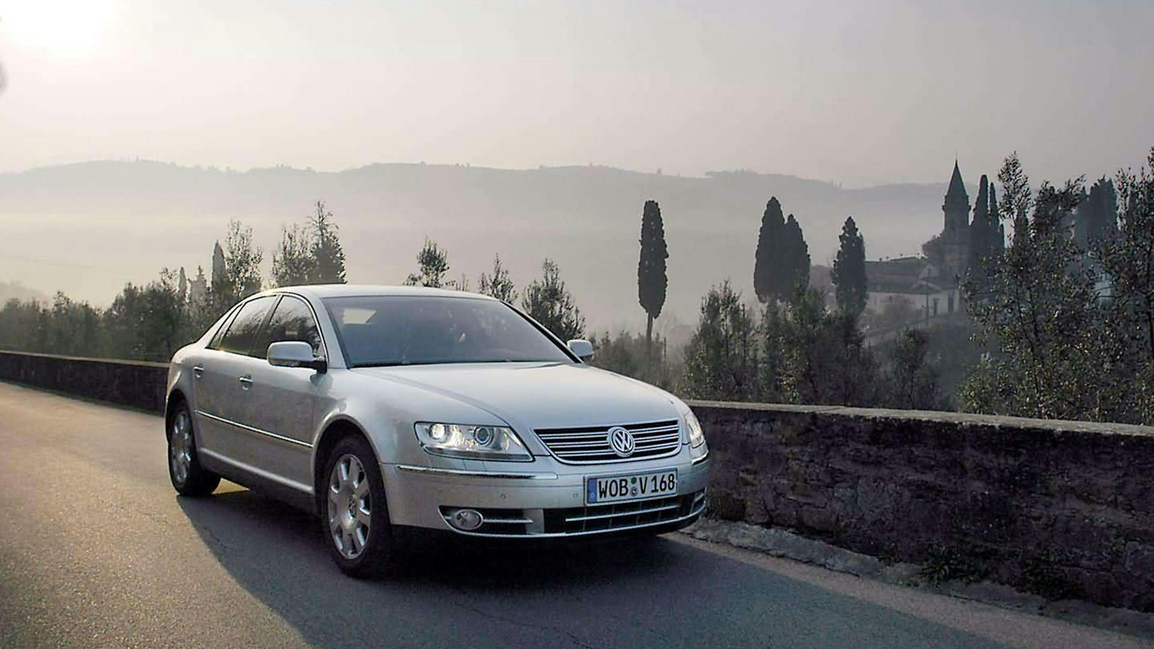 Ein silberner VW Phaeton fährt auf einer Landstraße an einer mediterranen Landschaft vorbei.