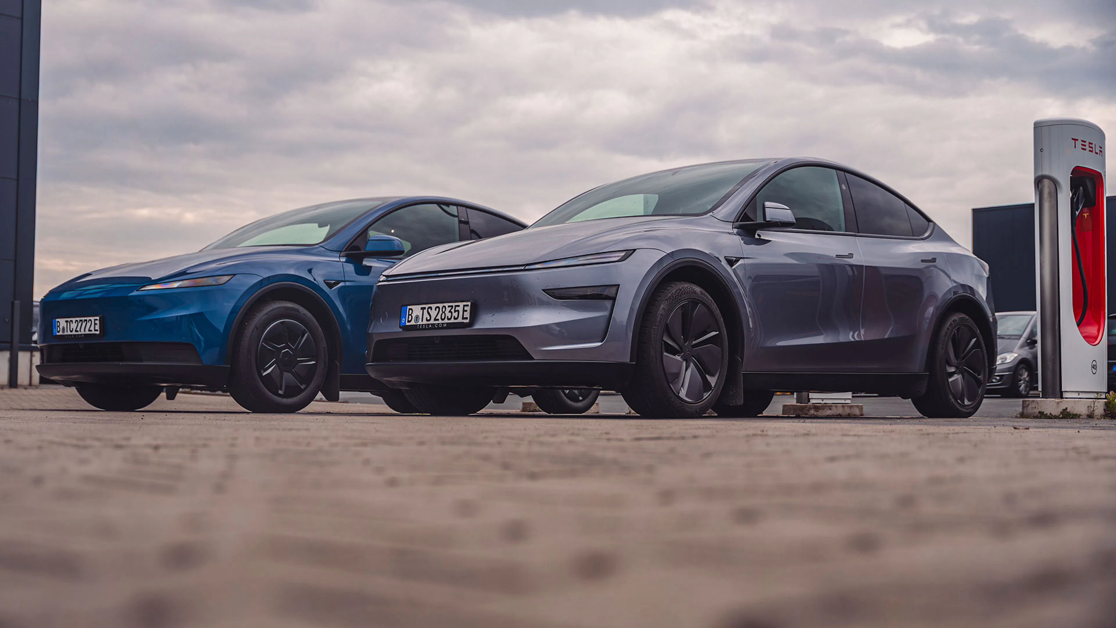 Ein blaues und ein graues Tesla Model Y stehen an einer Ladestation nebeneinander.