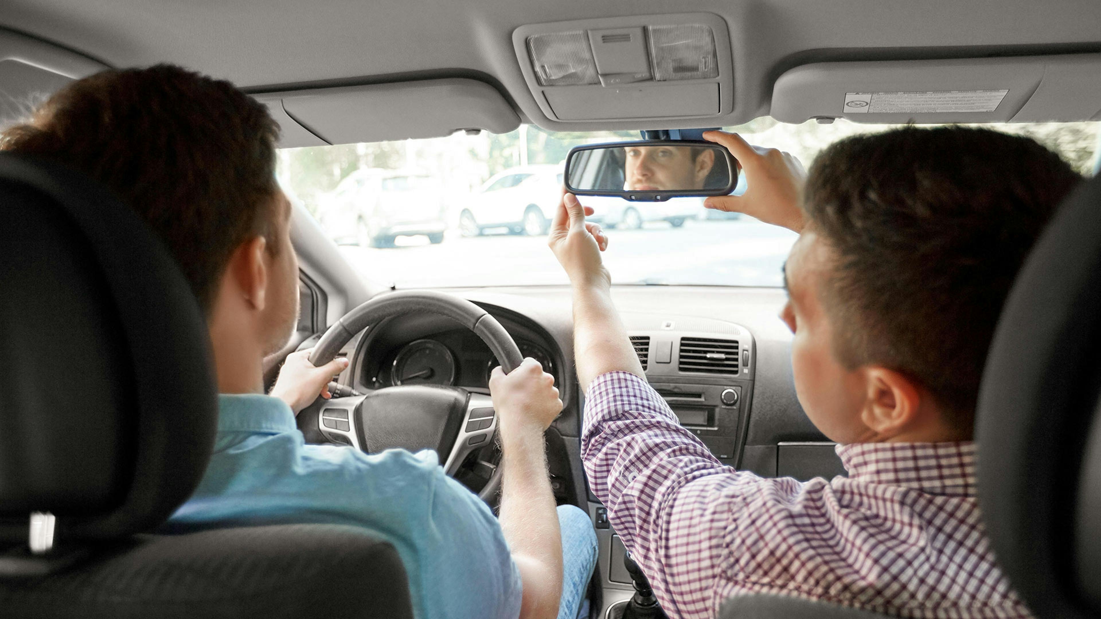 Rückansicht von zwei Männern, die in einem Auto sitzen und den Rückspiegel einstellen.