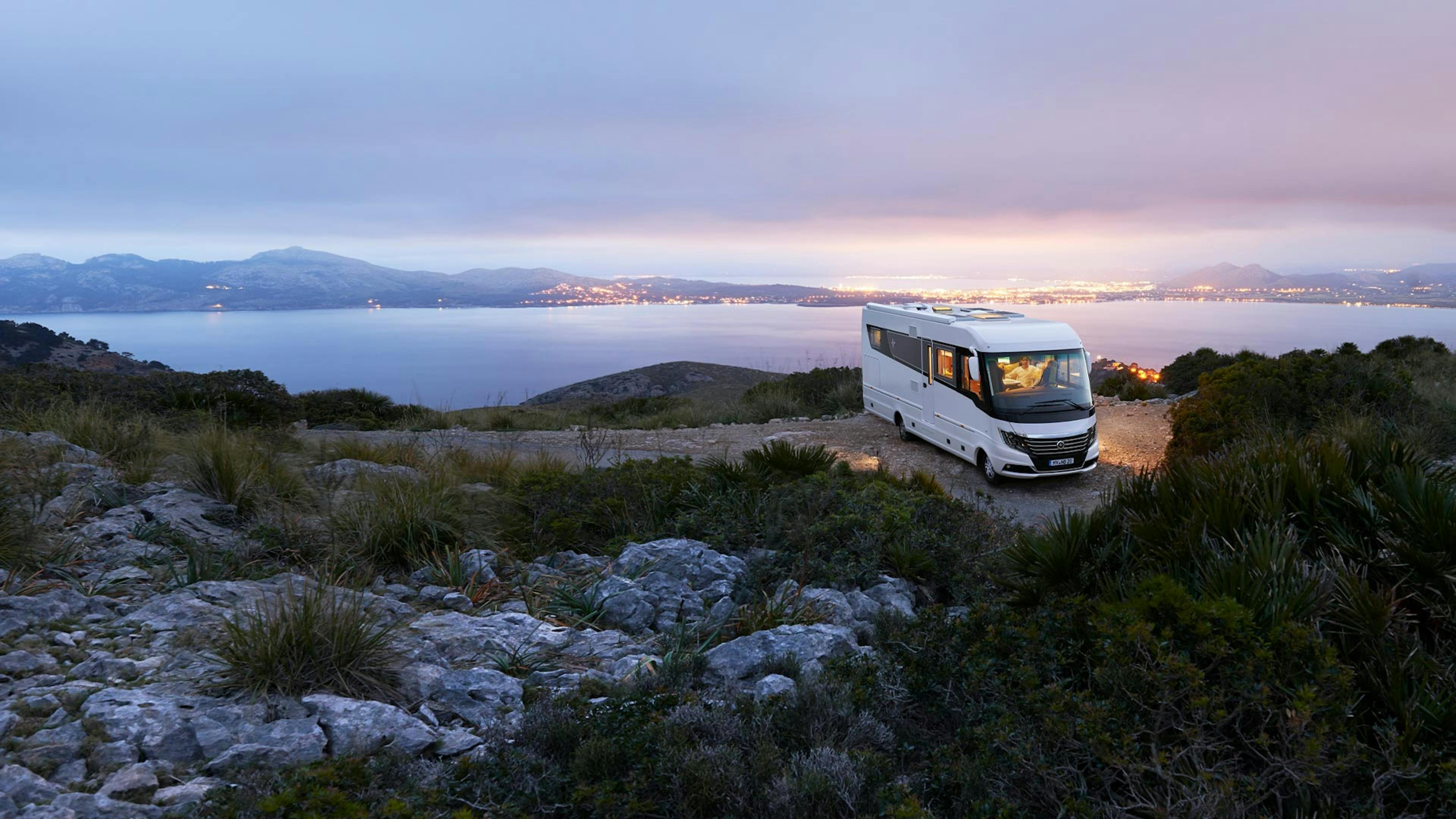 Ein Niesmann+Bischoff Wohnmobil Flair steht an einer Küste in einer mediterranen Landschaft im Sonnenuntergang.