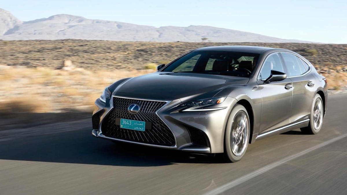 Ein silberner Lexus LS fährt eine Landstraße entlang durch eine karge Landschaft.