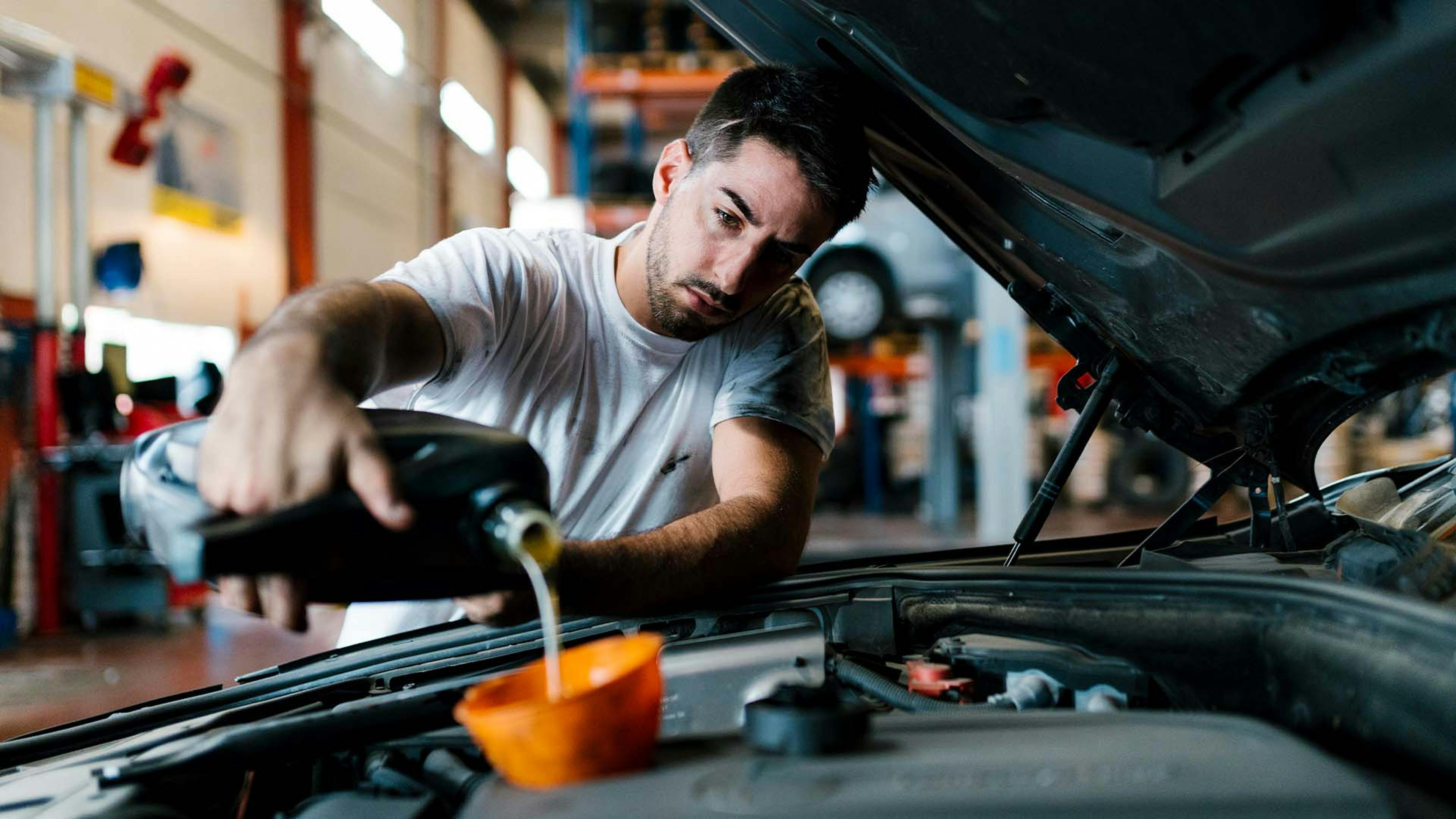 Ein Mechaniker in einer Werkstatt füllt Motoröl bei einem Pkw nach.
