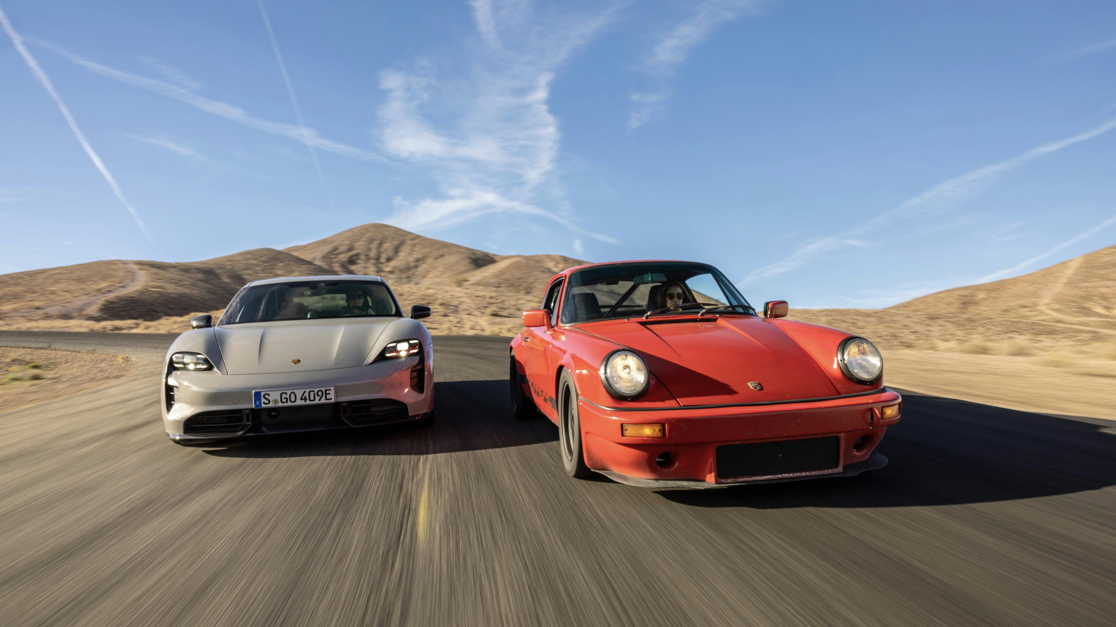 Frontansicht eines klassischen Porsche 911 und eines elektrischen Porsche Taycan, die nebeneinander auf der kalifornischen Rennstrecke "Willow Springs" fahren.