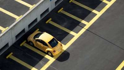 Draufsicht auf einen gelben Pkw, der auf einem Parkplatz mit gelben Spurmarkierungen steht