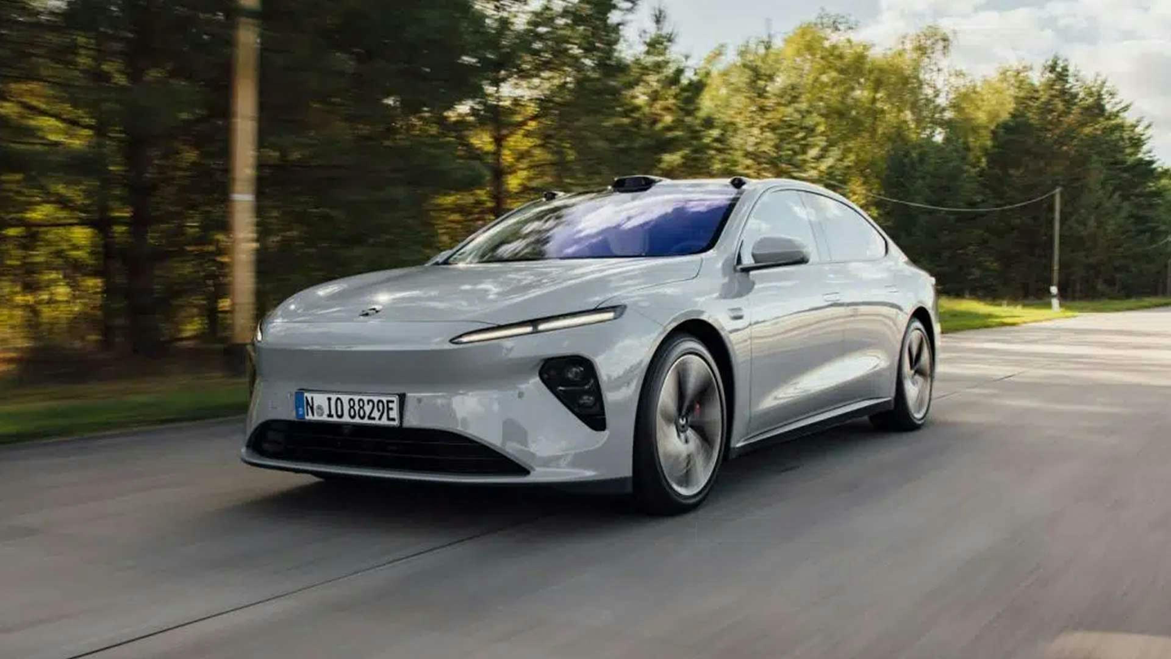 Ein silbernes Nio ET7 Elektroauto fährt eine Landstraße entlang, an einem Waldstück vorbei.