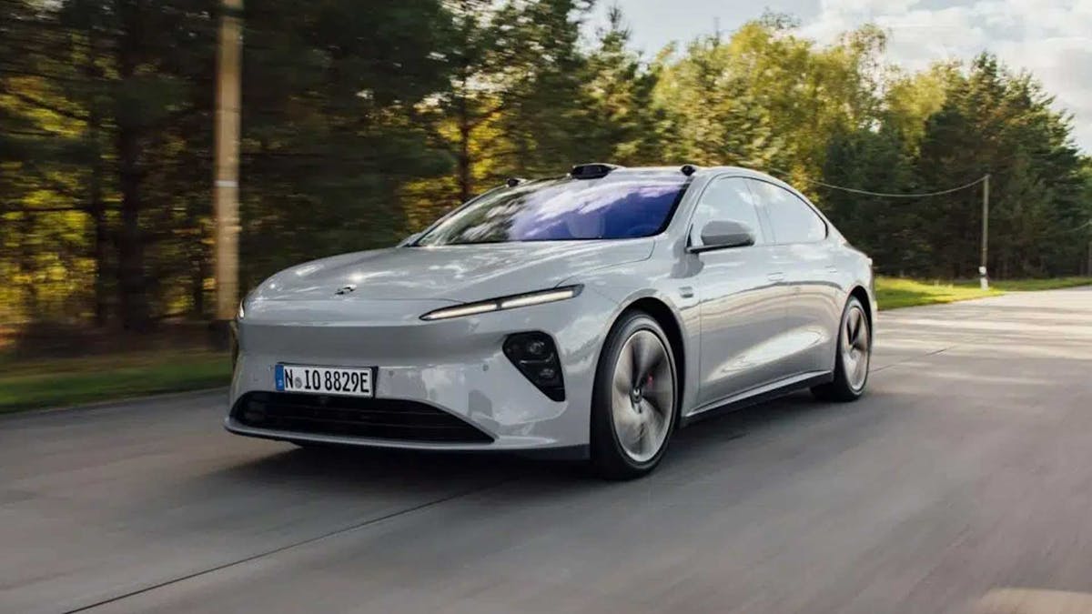 Ein silbernes Nio ET7 Elektroauto fährt eine Landstraße entlang, an einem Waldstück vorbei.