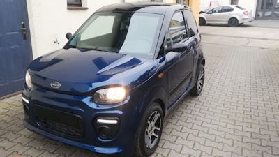 Ein blaues M.Go Microcar steht in einer Einfahrt.
