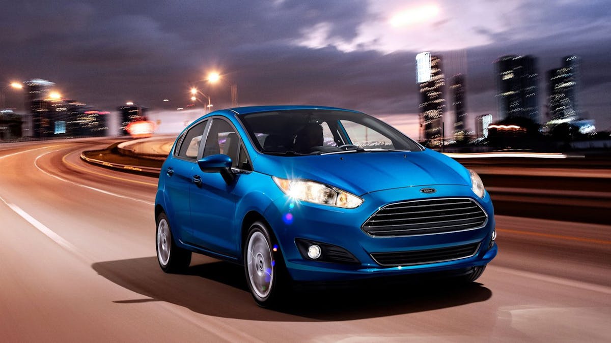 Ein blauer Ford Fiesta fährt durch eine Stadt im Abendlicht.