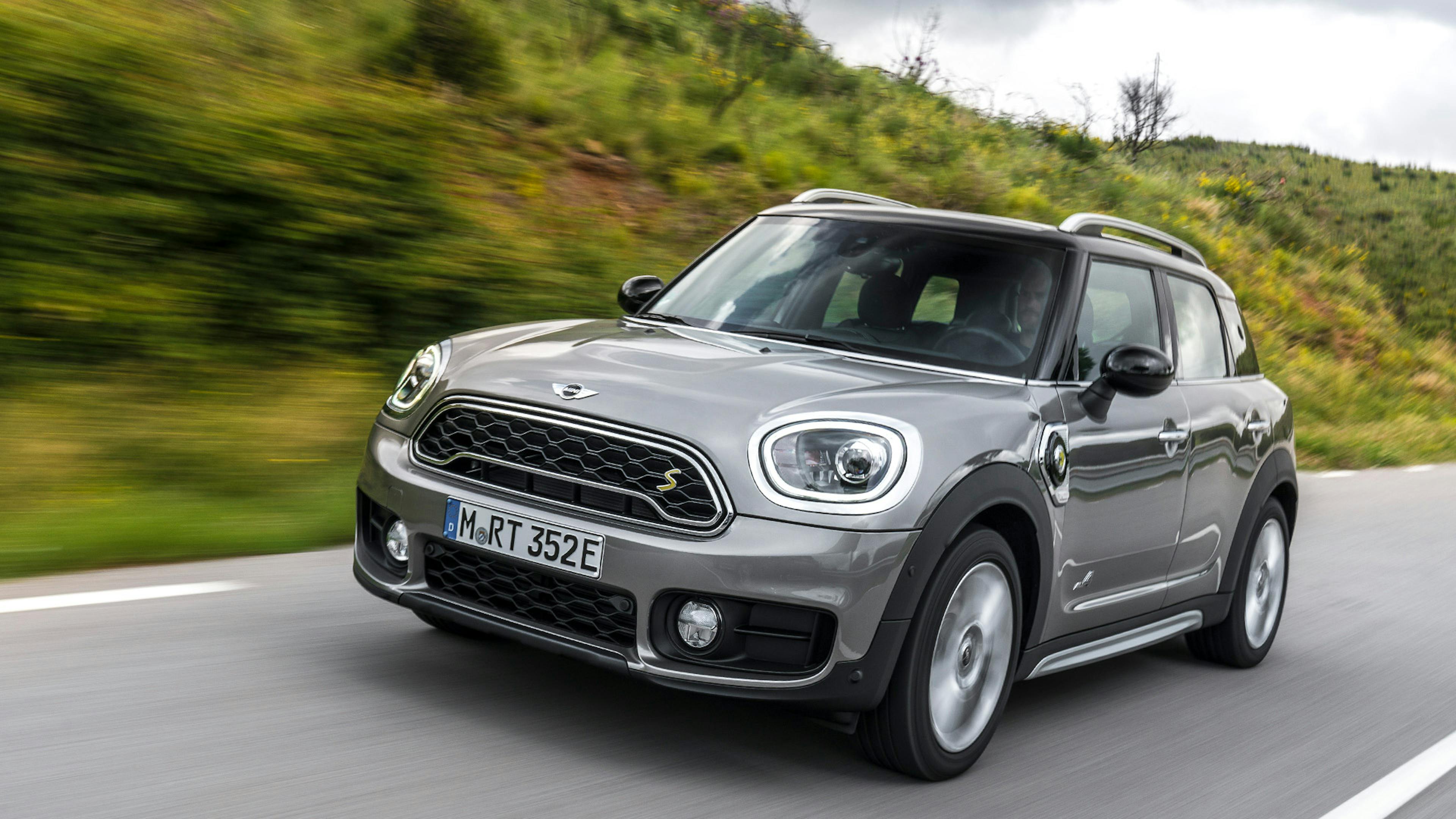 Ein grauer Mini Countryman SE Plug-in-Hybrid fährt eine Landstraße entlang