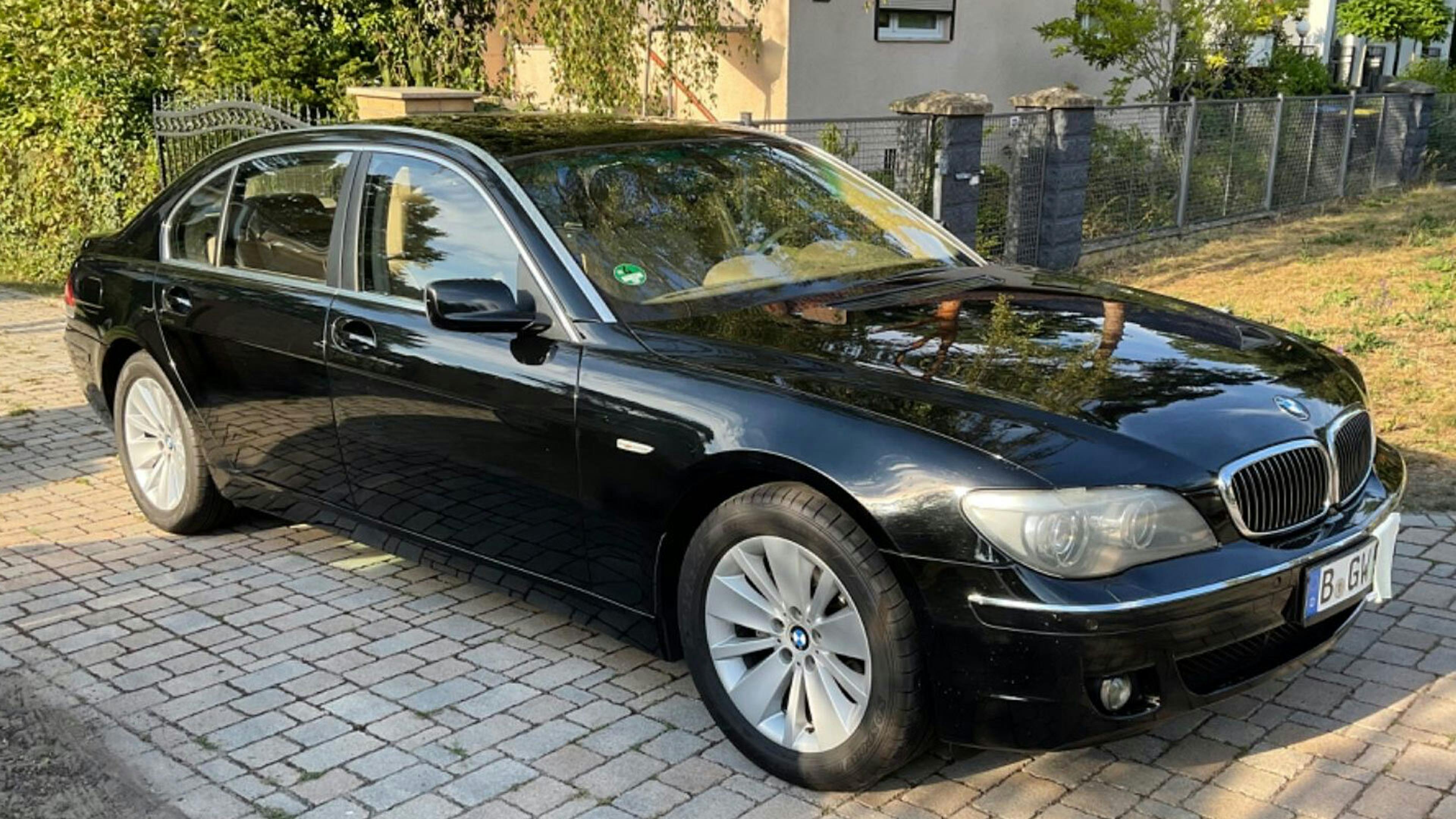 Ein schwarzer BMW 7er steht vor einem Haus in der Auffahrt.