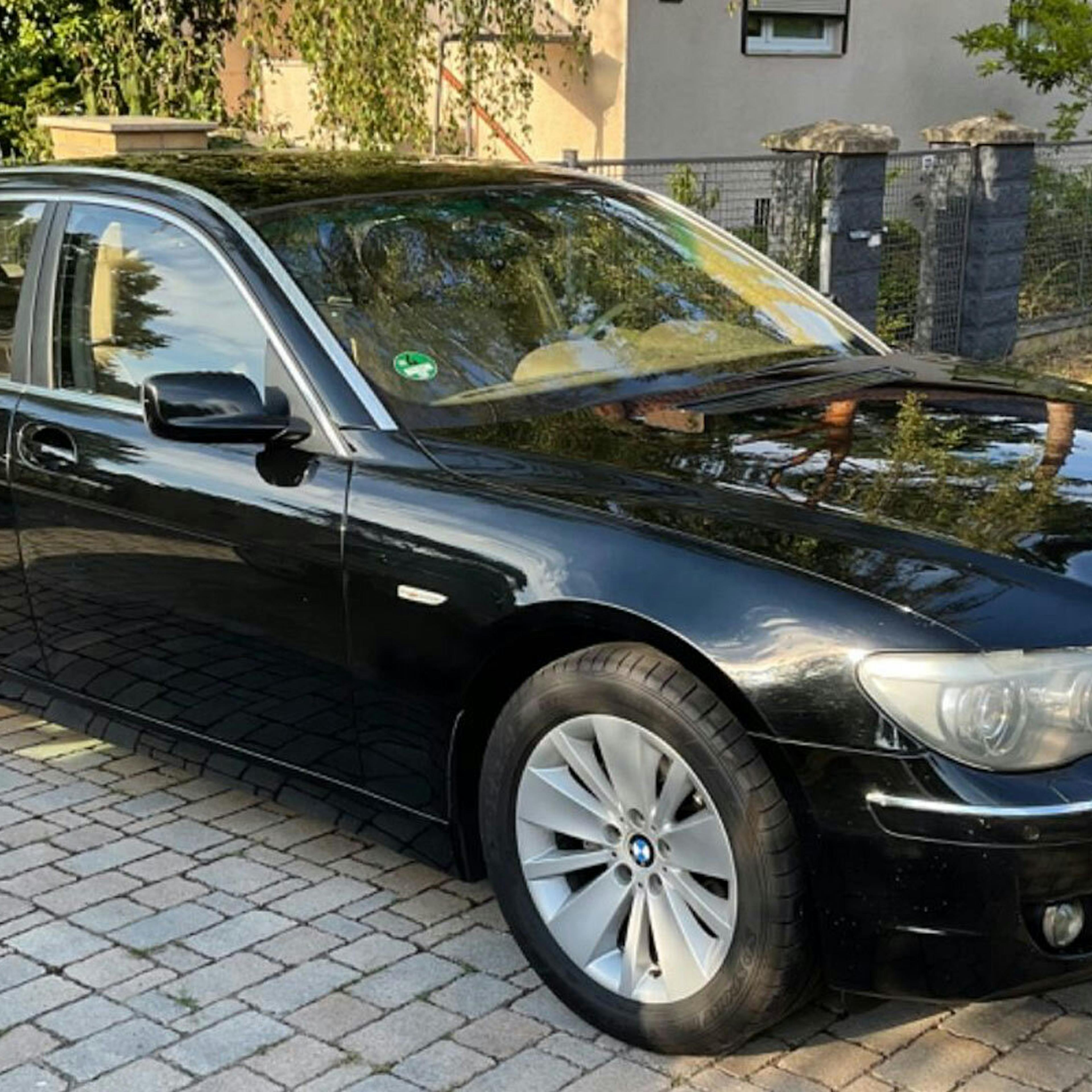Ein schwarzer BMW 7er steht vor einem Haus in der Auffahrt.