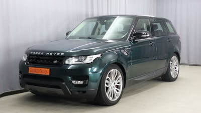 Ein dunkelgrüner Land Rover Range Rover Sport 3.0 225 kW steht vor einem grauen Vorhang.