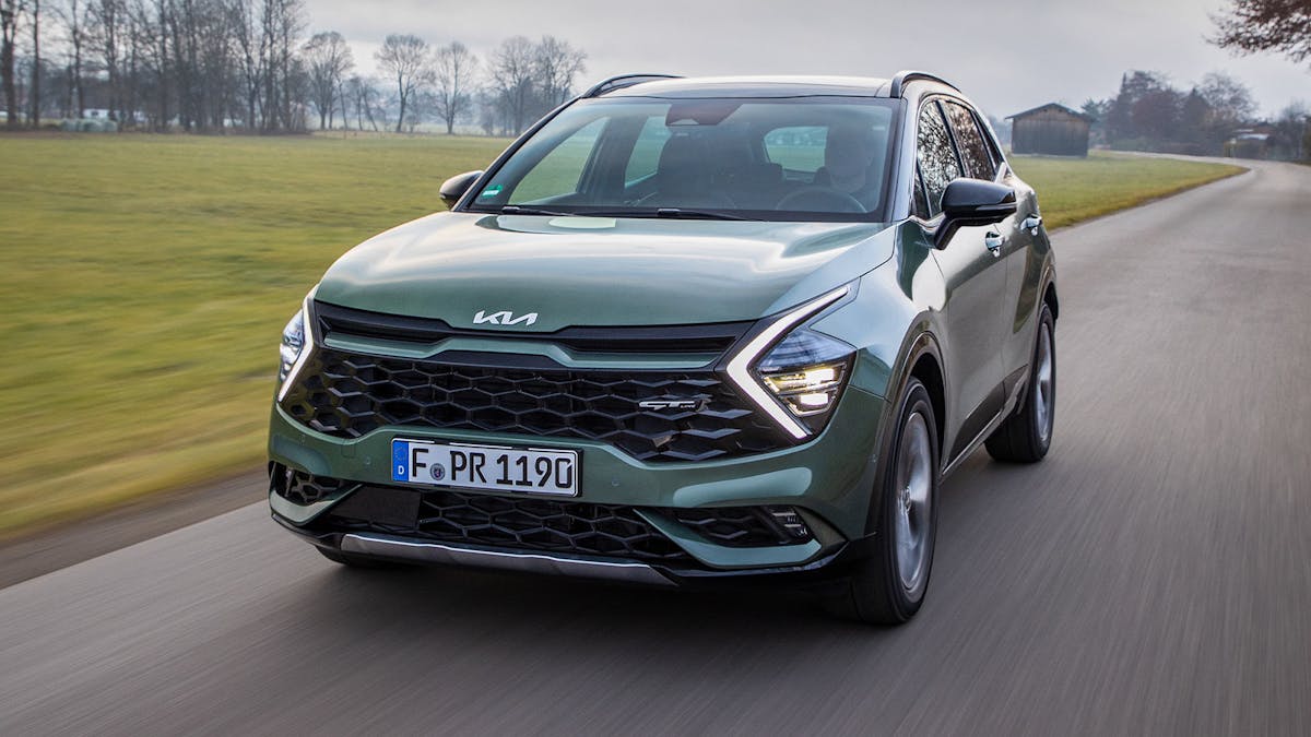 Ein grüner Kia Sportage fährt eine Landstraße entlang.