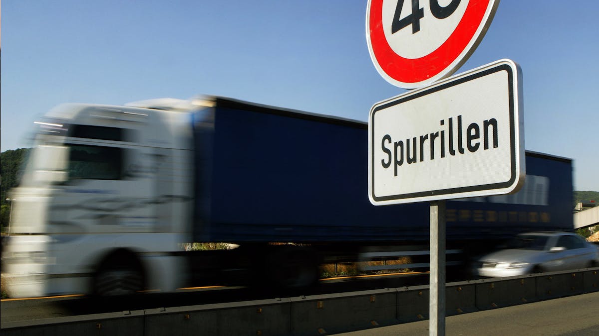 Ein Lkw und ein Pkw fahren an einem Verkehrszeichen vorbei, das auf Spurrillen und die damit verbundene Gefahr durch Aquaplaning hinweist.