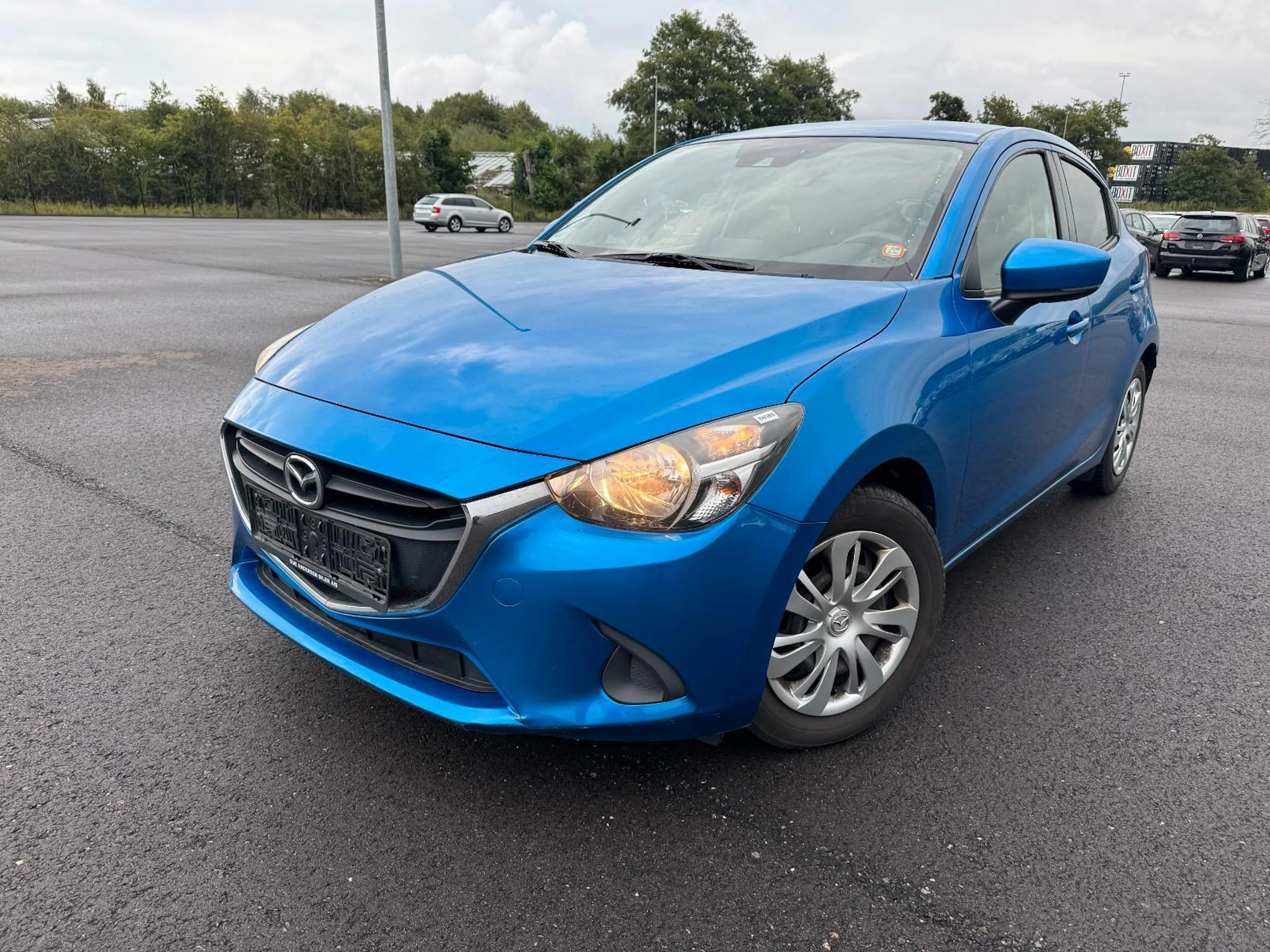 Ein blauer Mazda2 steht auf einer asphaltierten Fläche.
