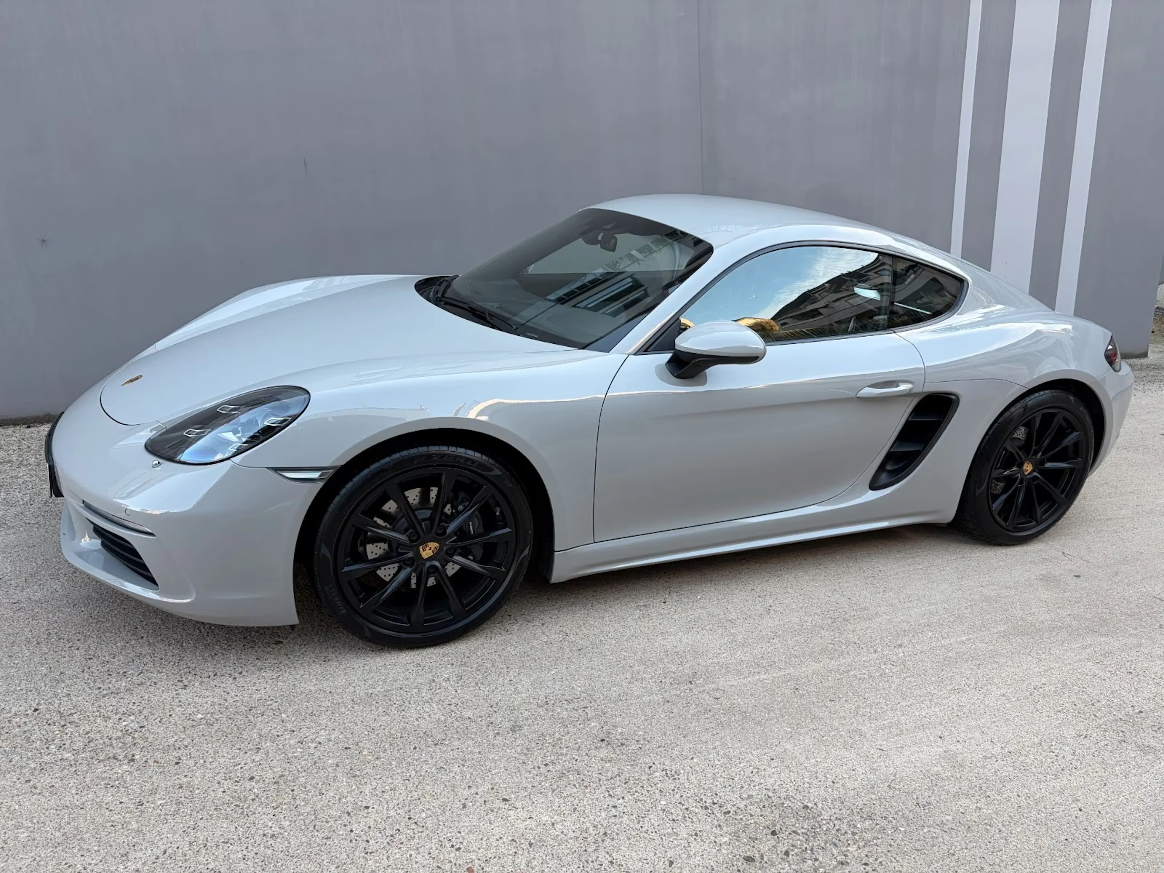 Ein grauer Porsche Cayman steht auf einer befestigten Fläche.