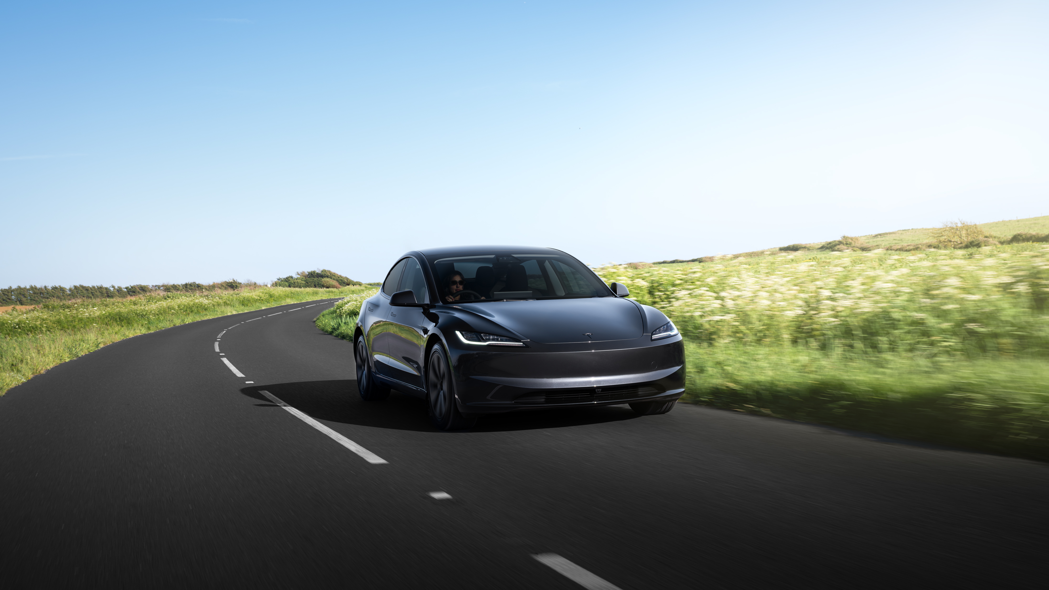 Ein schwarzer Tesla Model 3 fährt auf einer Landstraße.