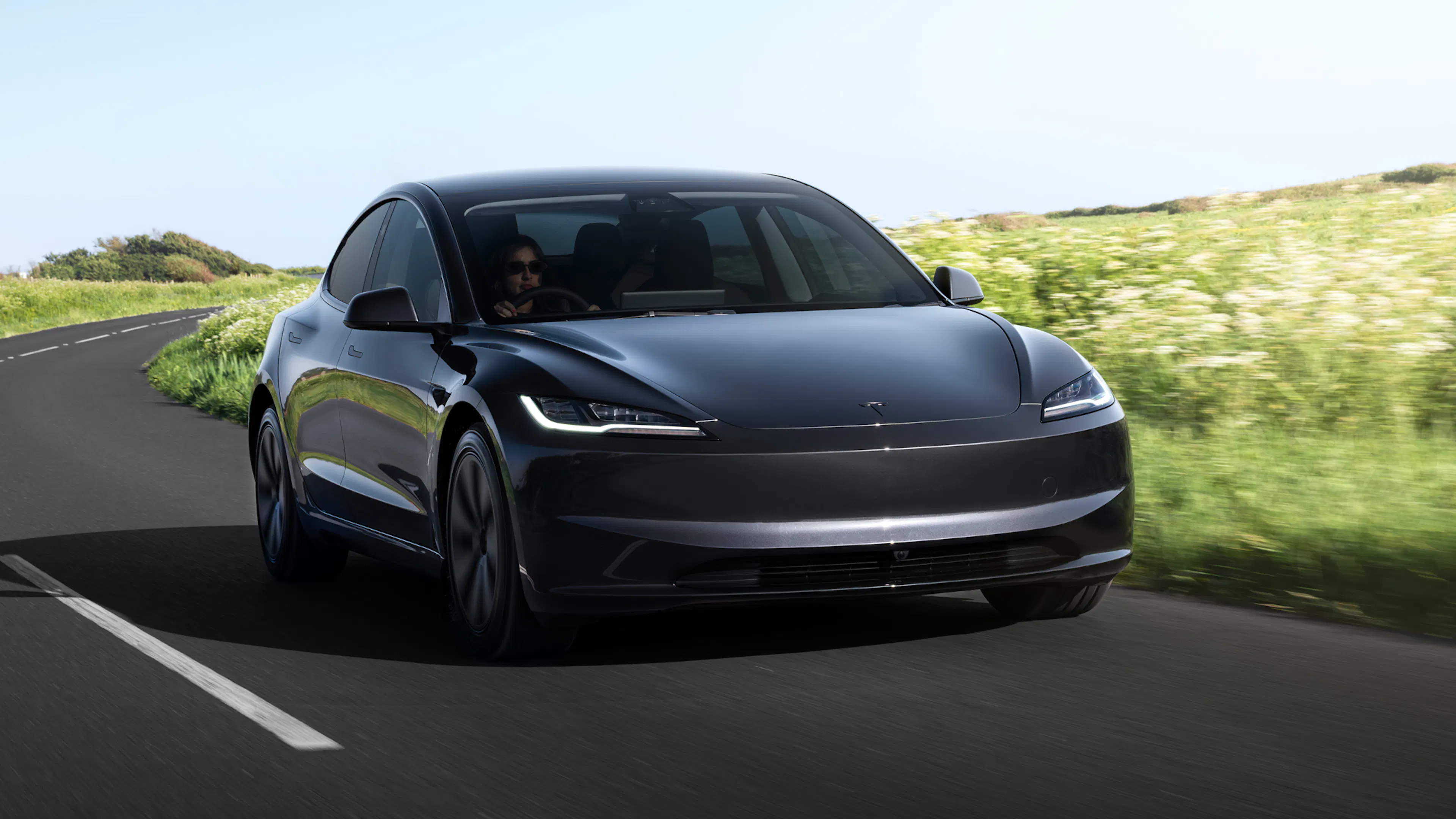 Ein schwarzer Tesla Model 3 fährt auf einer Landstraße.
