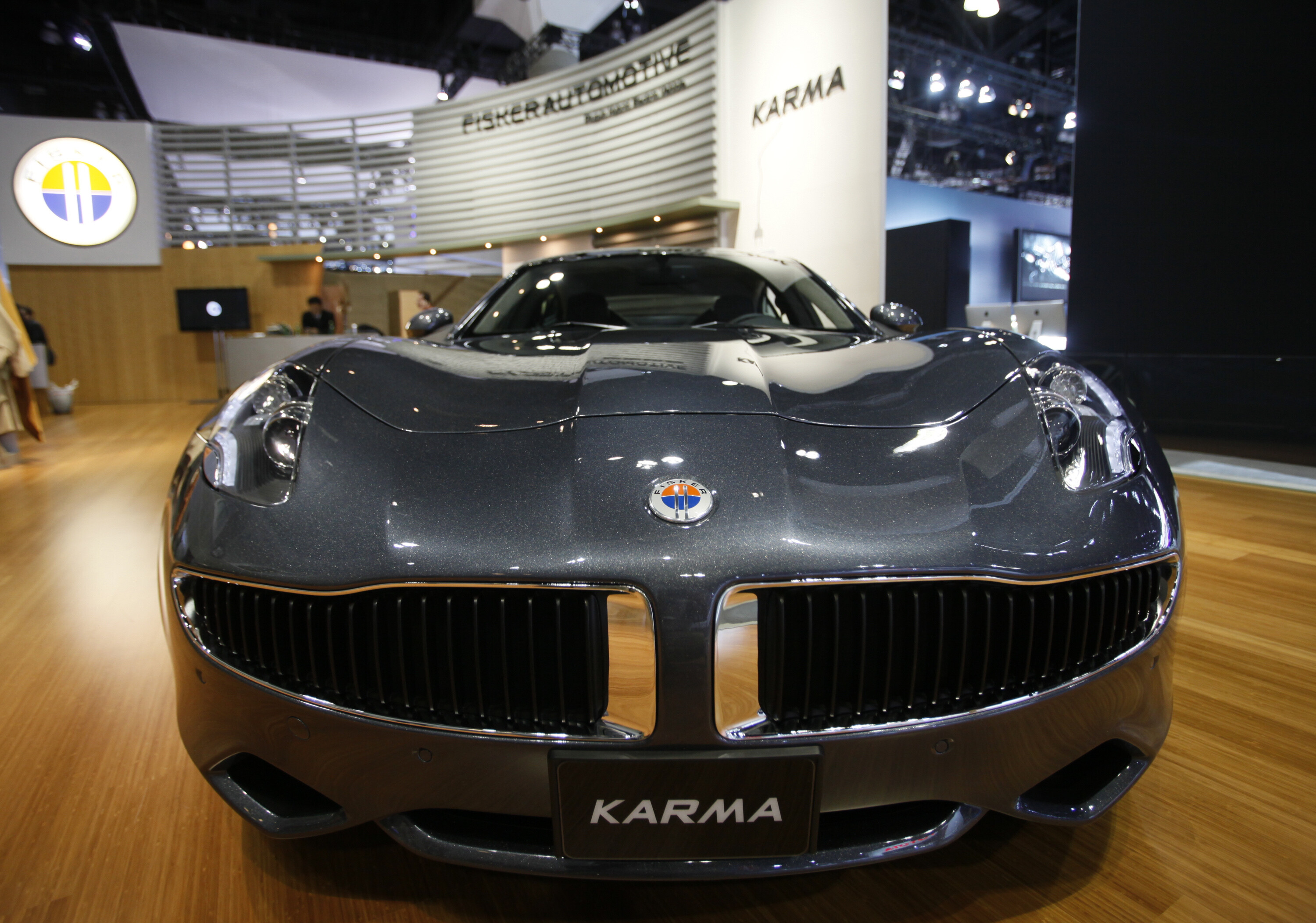 Dunkelgrauer Fisker Karma auf einer Automesse in Frontansicht, Messestand mit Fisker-Automotive-Logo im Hintergrund.
