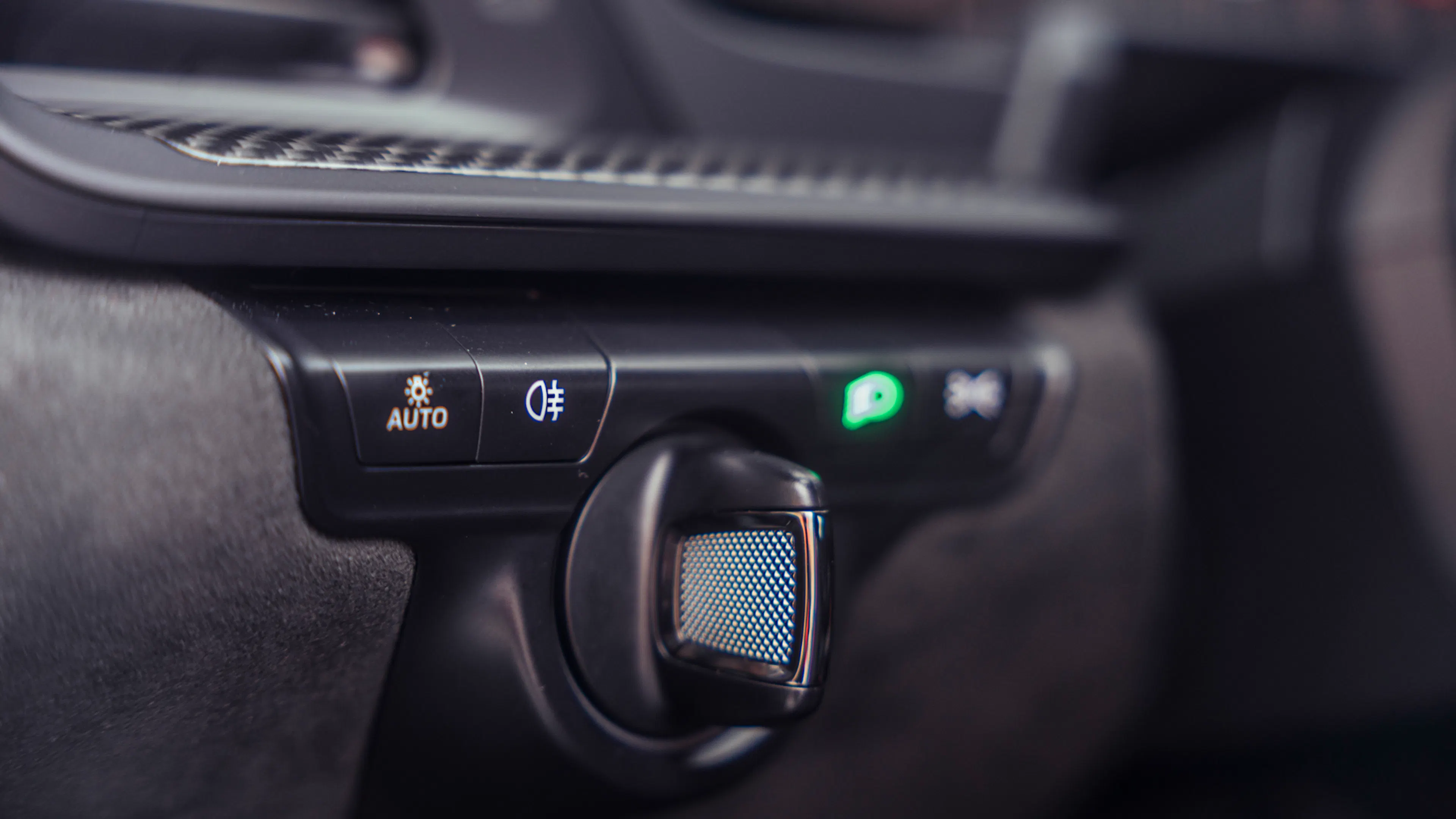 Nahaufnahme der Bedienelemente im Cockpit des Porsche 911 GT3 mit Lichtautomatik, Nebelleuchtensymbol und Drehregler auf schwarzer Verkleidung.
