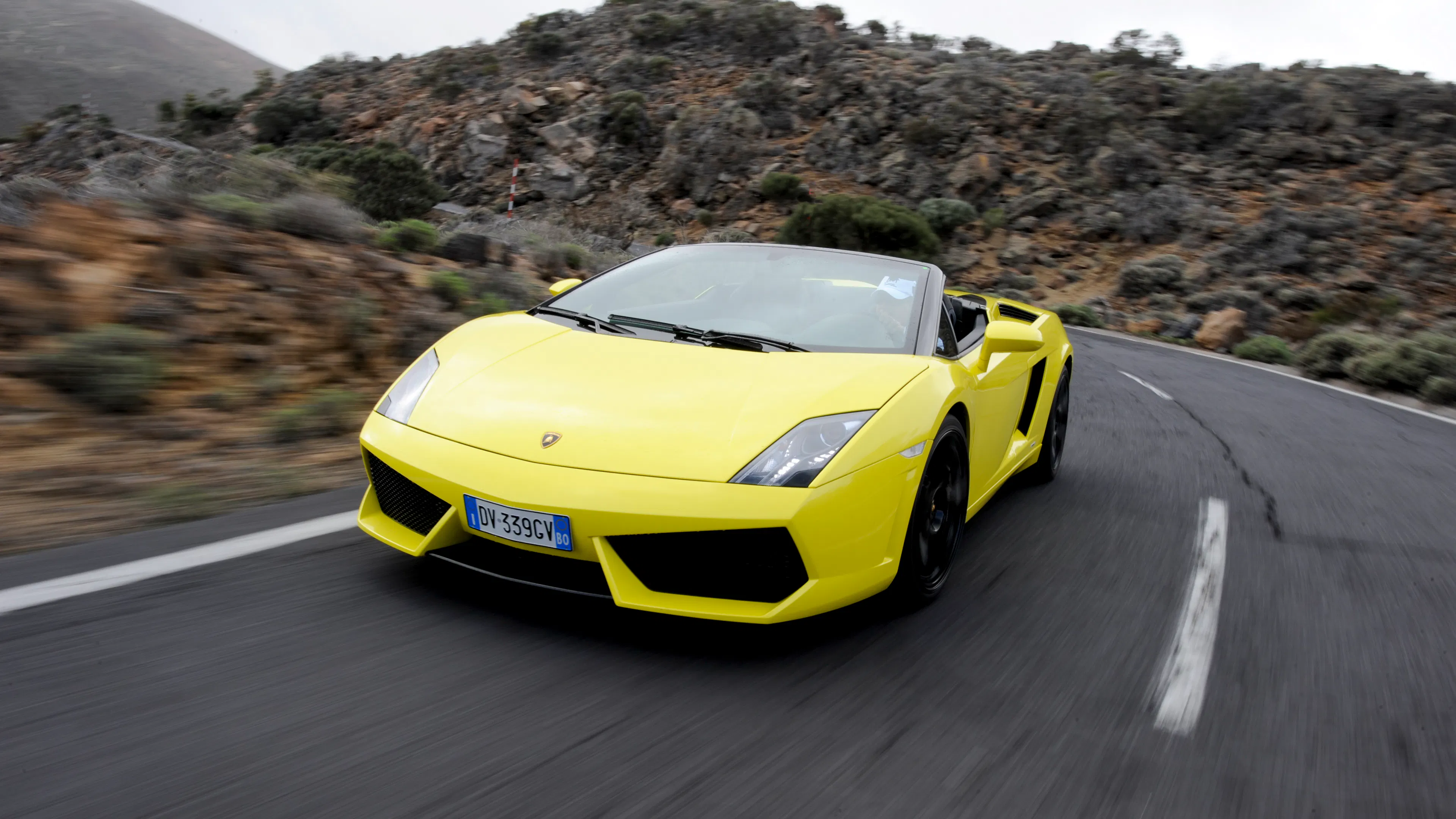 Ein neongelber Lamborghini Gallardo Spyder fährt auf einer Landstraße.