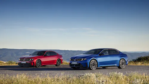 Zwei BMW Limousinen, eine rote und eine blaue, nebeneinander auf einer Bergstraße