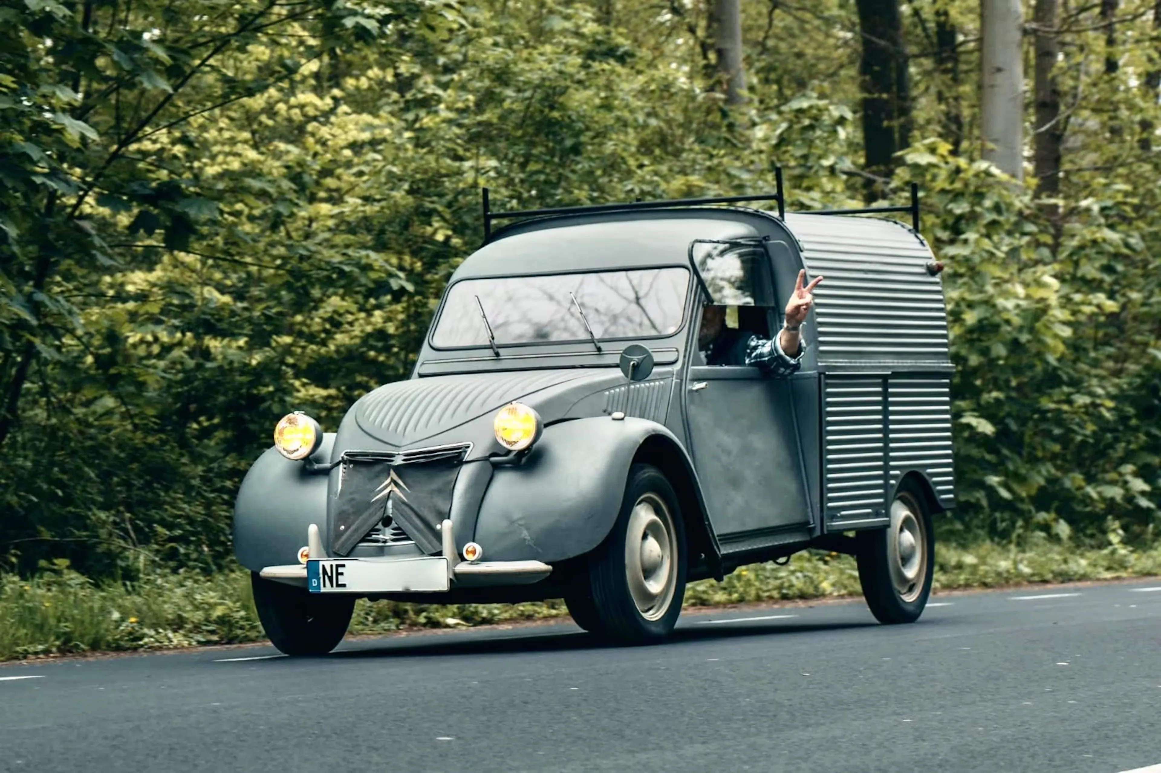 Eine graue Citroën-2CV-Kastenente fährt auf einer Landstraße