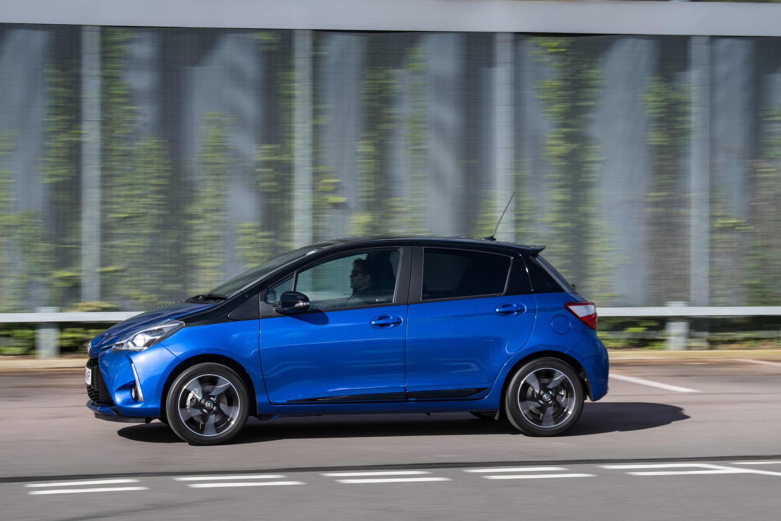 Blauer Toyota Yaris mit schwarzem Dach in der Seitenansicht während der Fahrt.