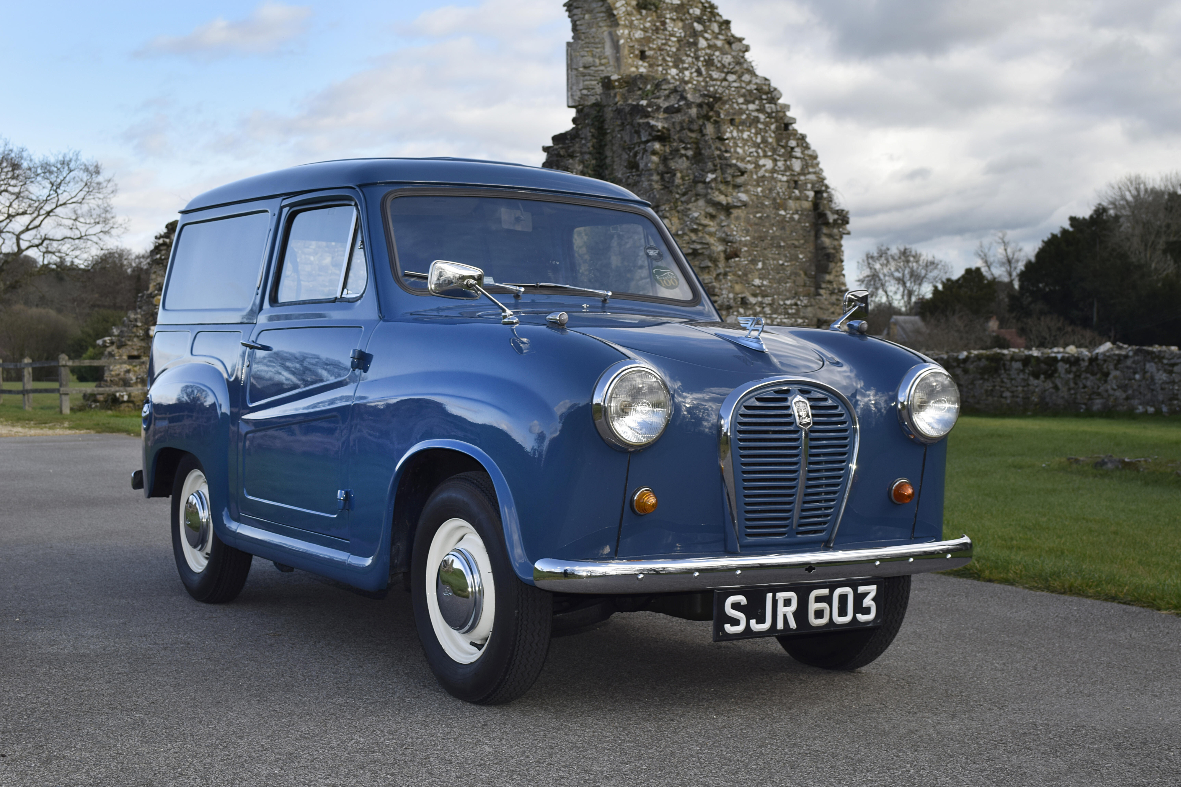 Blauer Austin A35 Van in Dreiviertel-Frontansicht, geparkter Oldtimer vor einer Ruine