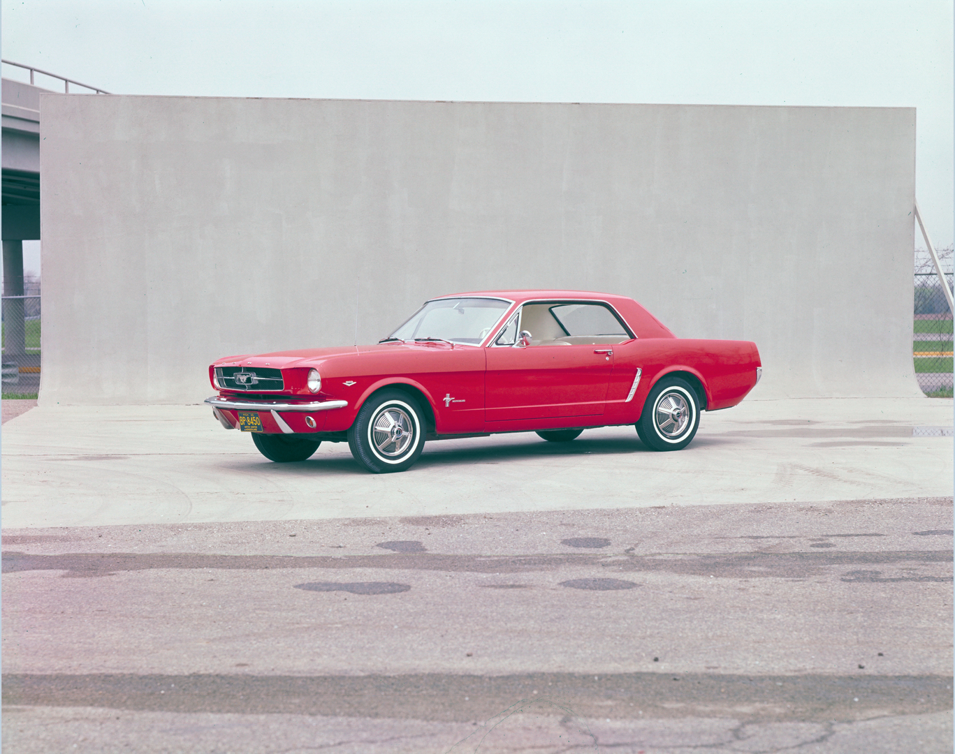 Roter Ford Mustang 1965 Hardtop Coupé in seitlicher Studioaufnahme vor neutralem Hintergrund.