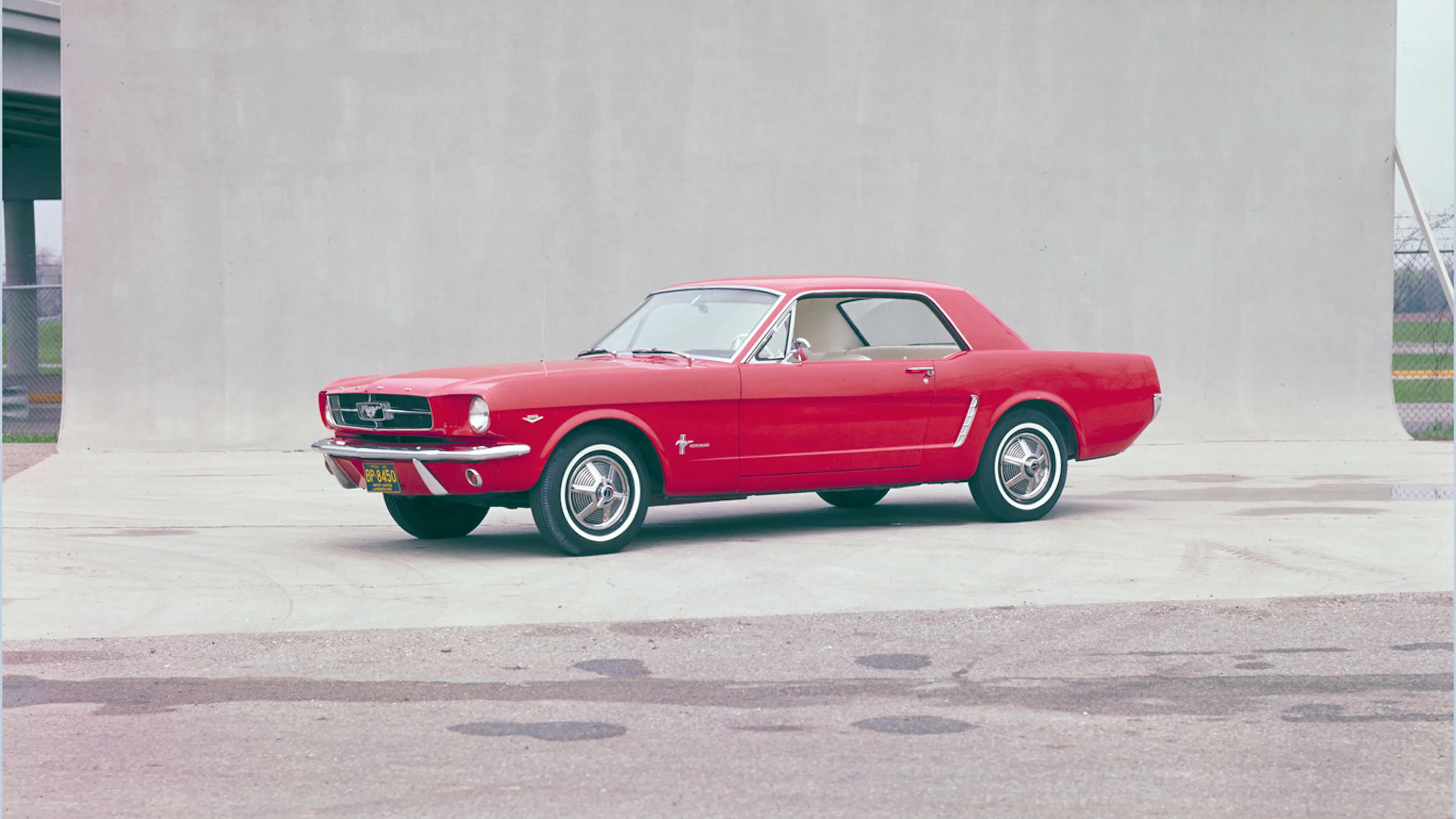 Roter Ford Mustang 1965 Hardtop Coupé in seitlicher Studioaufnahme vor neutralem Hintergrund.