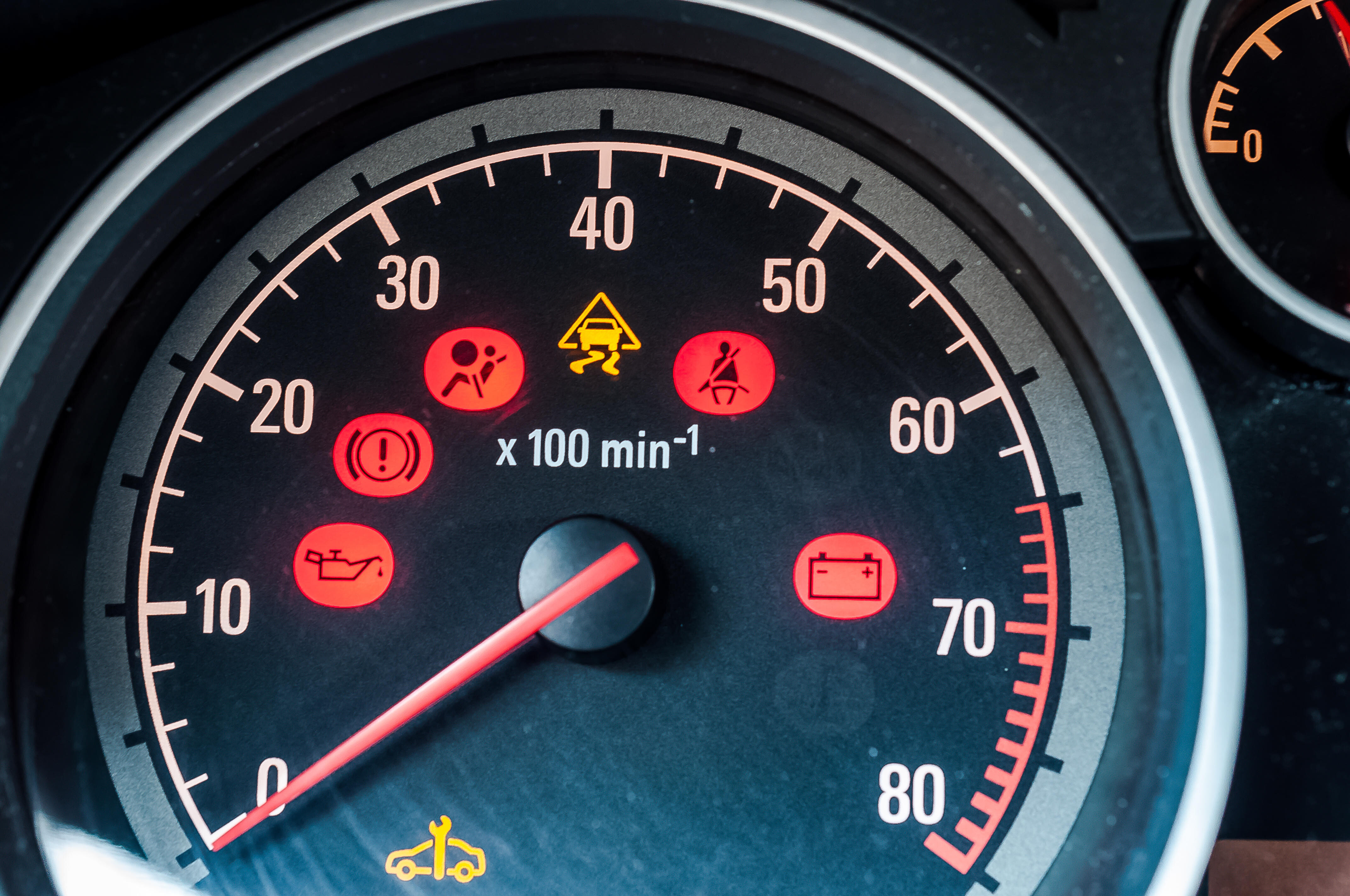 Tachometer eines Autos mit mehreren leuchtenden Warnleuchten und einem gelben Inspektionssymbol.