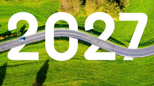 Luftaufnahme einer Landstraße, die sich durch grüne Wiesen schlängelt, mit einem kleinen blauen Auto und der großen weißen Zahl 2027 im Vordergrund