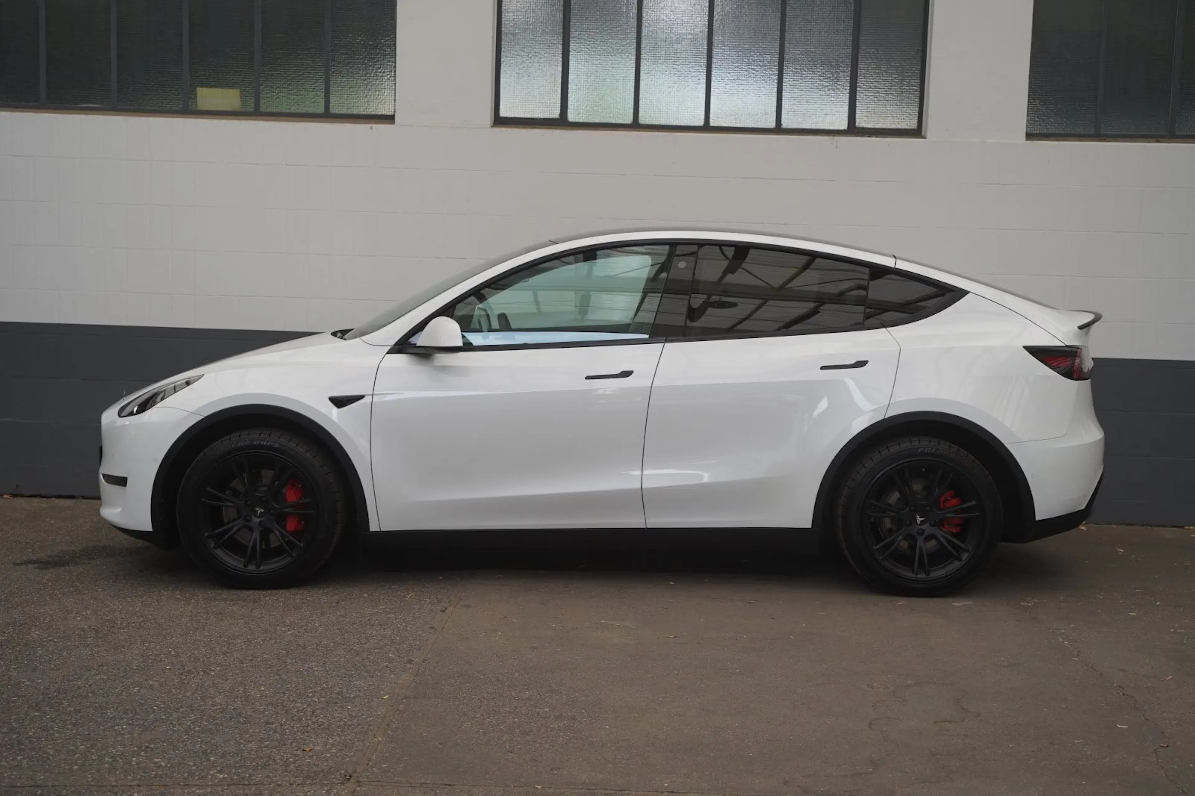 Ein weißes Tesla Model Y steht vor einer Hauswand mit Fenstern.