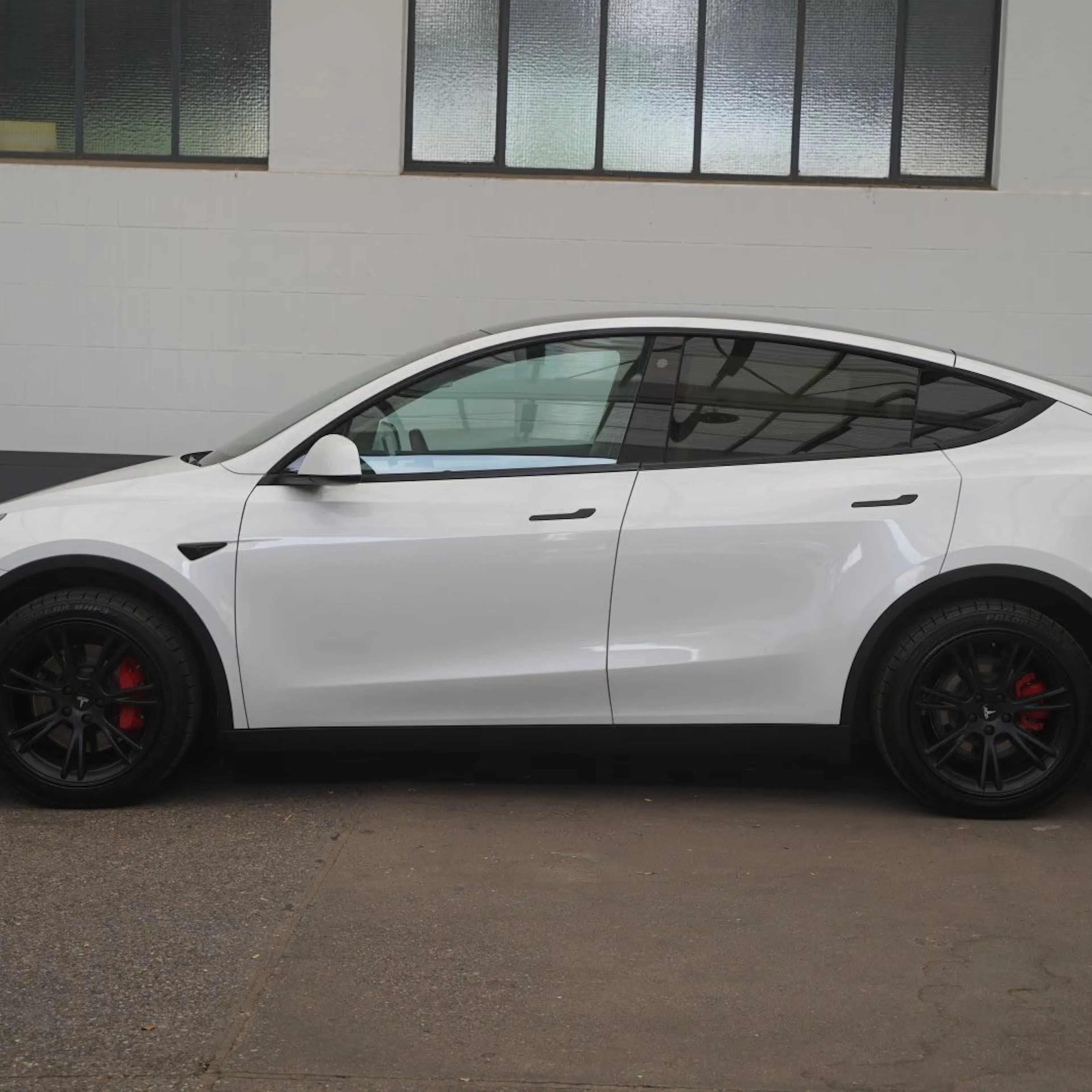 Ein weißes Tesla Model Y steht vor einer Hauswand mit Fenstern.