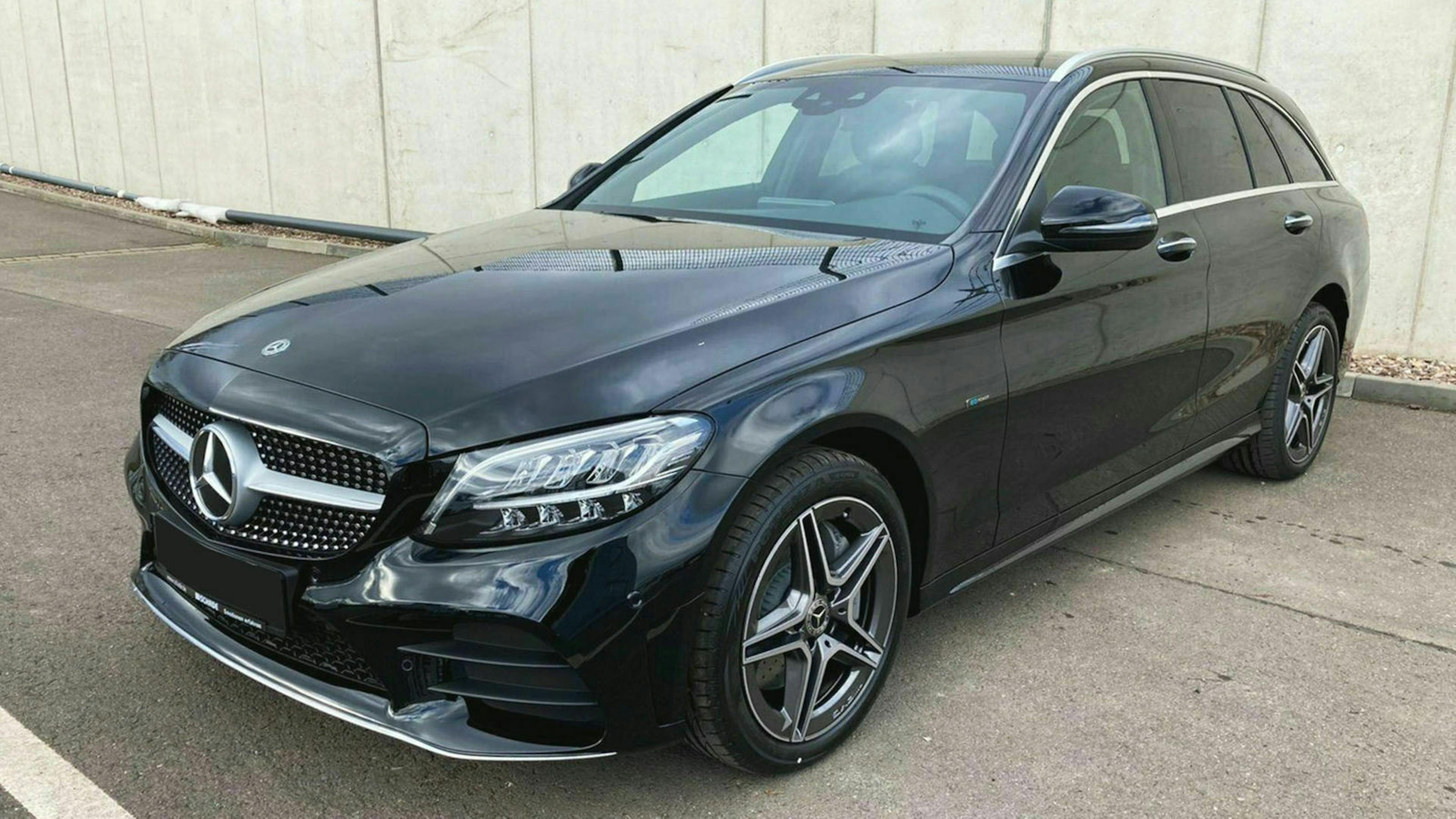 Ein schwarzer Mercedes-Benz E 300 de T-Modell steht auf einem Parkplatz vor einer hellgrauen Wand