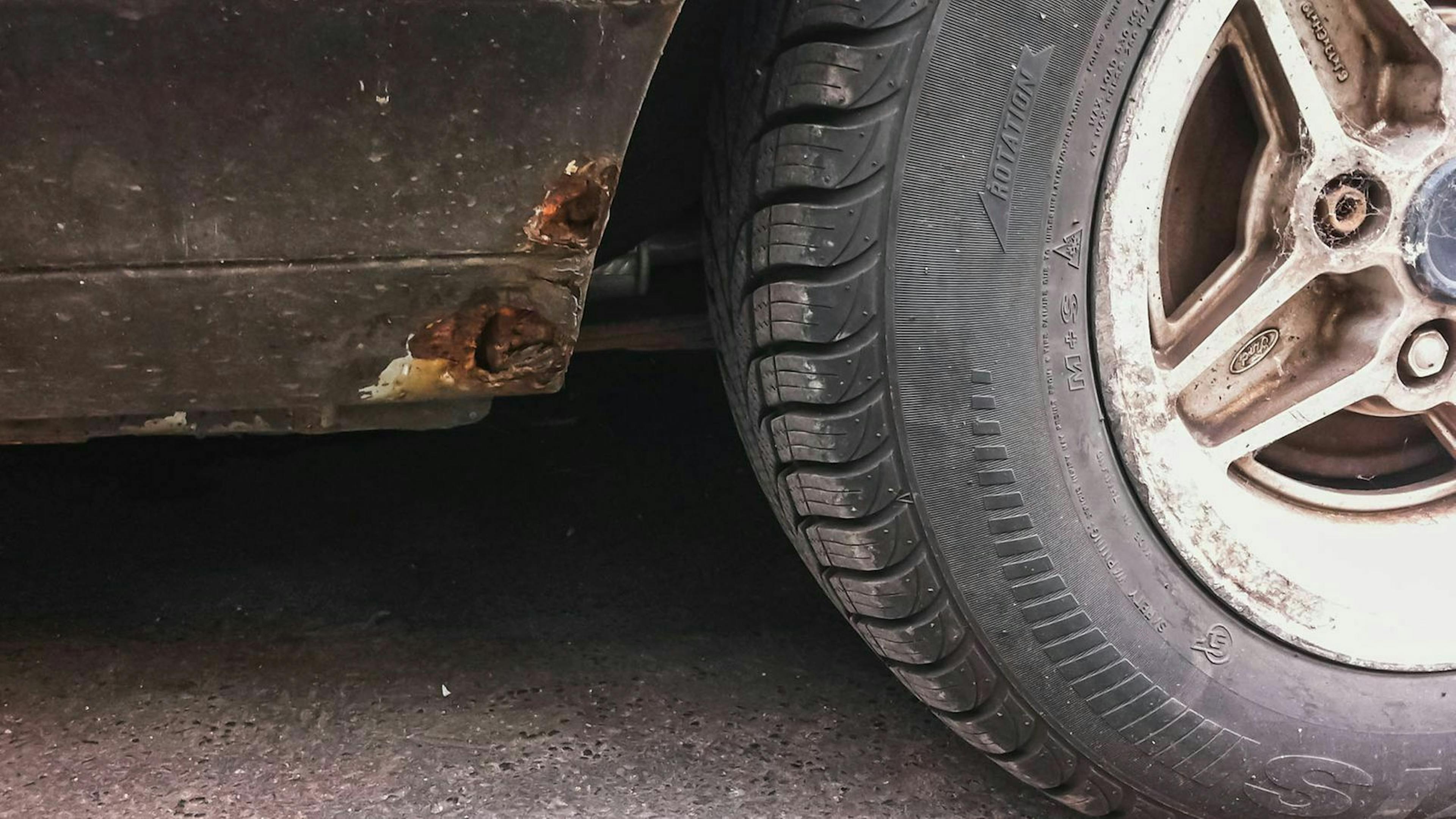 In Nahaufnahme ist ein Rostloch am Seitenschweller eines Autos zu sehen.