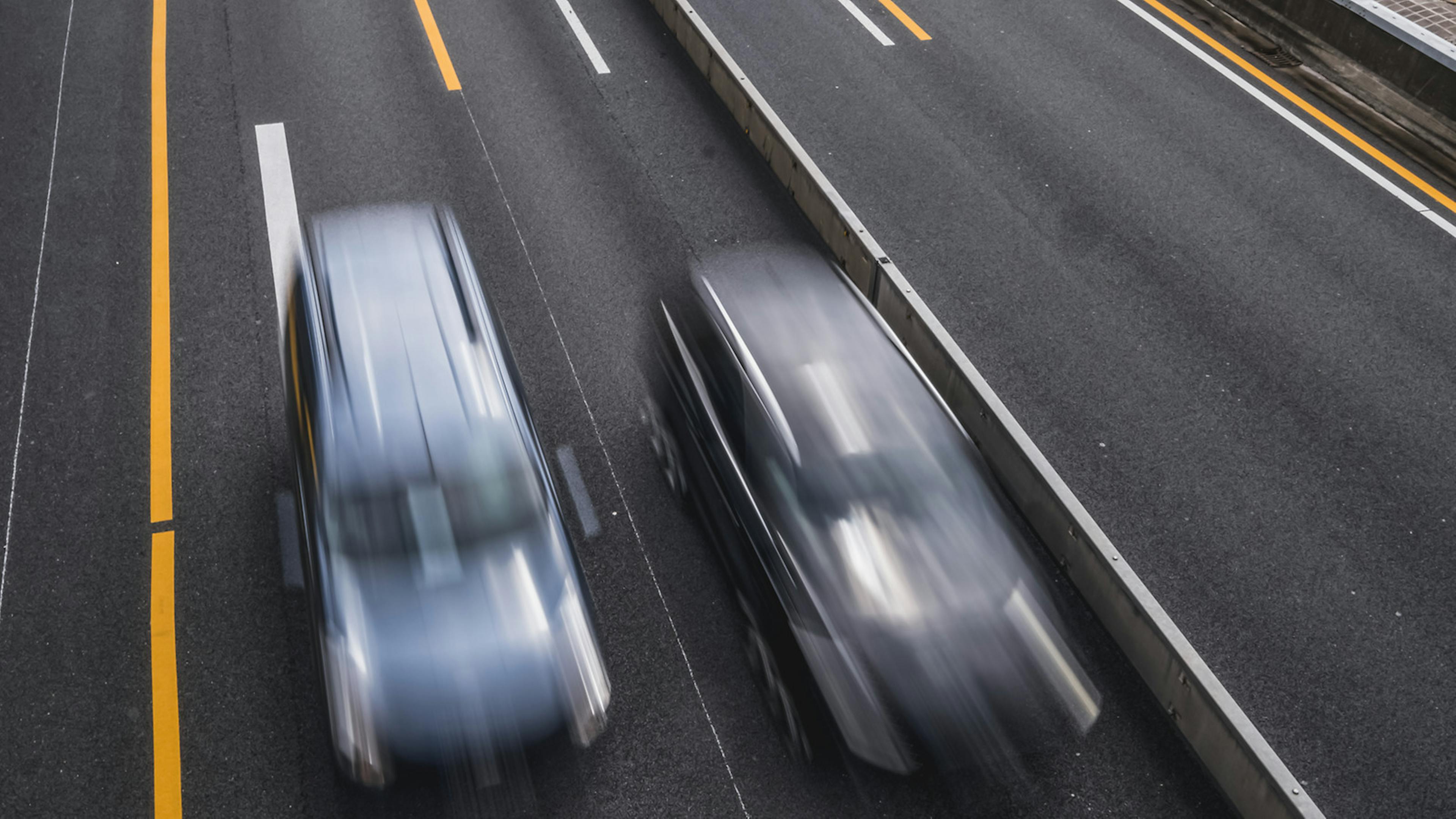 Zwei Autos fahren auf der Autobahn. Durch die längere Belichtungszeit verschwimmen ihre Konturen.