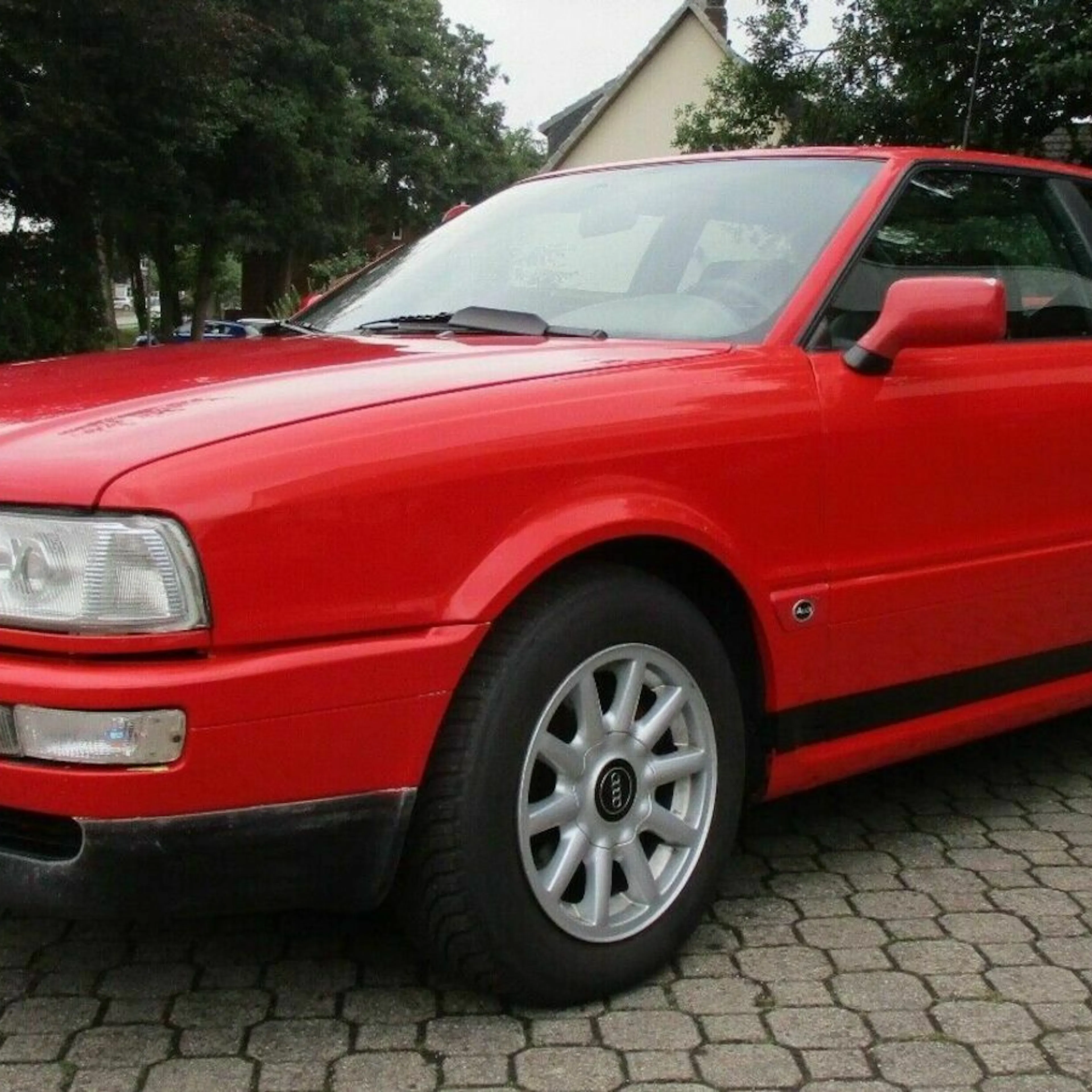 Ein roter Audi Coupé Quattro Oldtimer steht auf einem Parkplatz vor einem Haus.