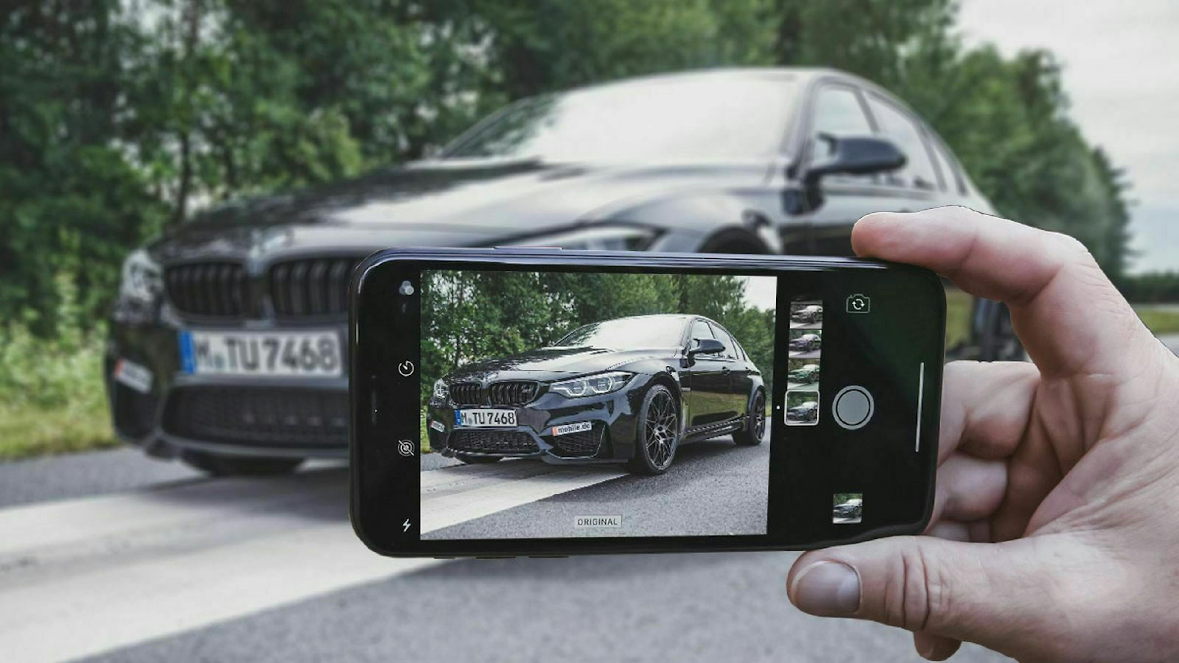 Jemand fotografiert mit einem Handy ein Auto.