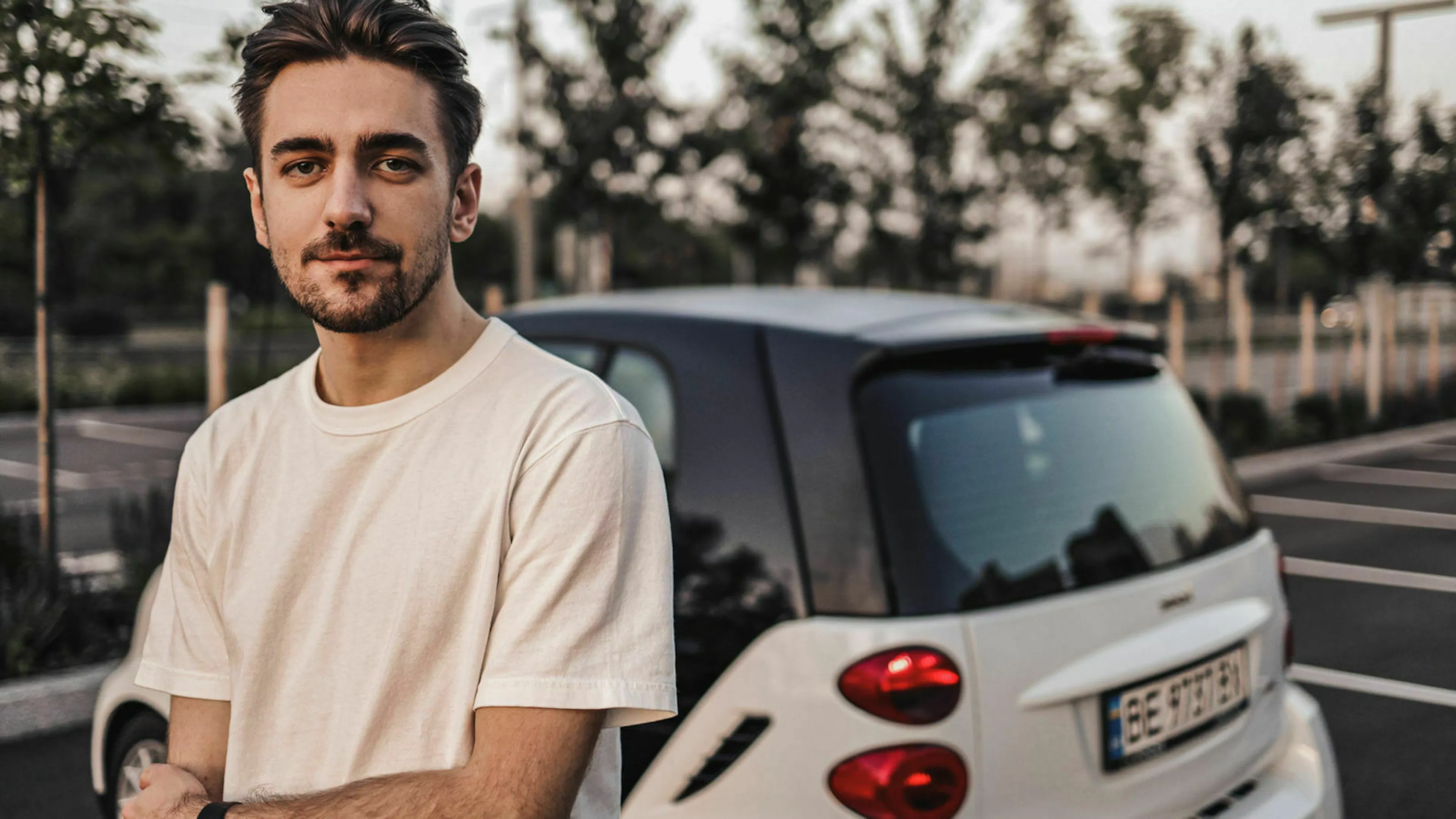 Jemand steht nachdenklich vor einem weißen Kleinwagen und überlegt, ob ein Auto-Abo eine Alternative wäre