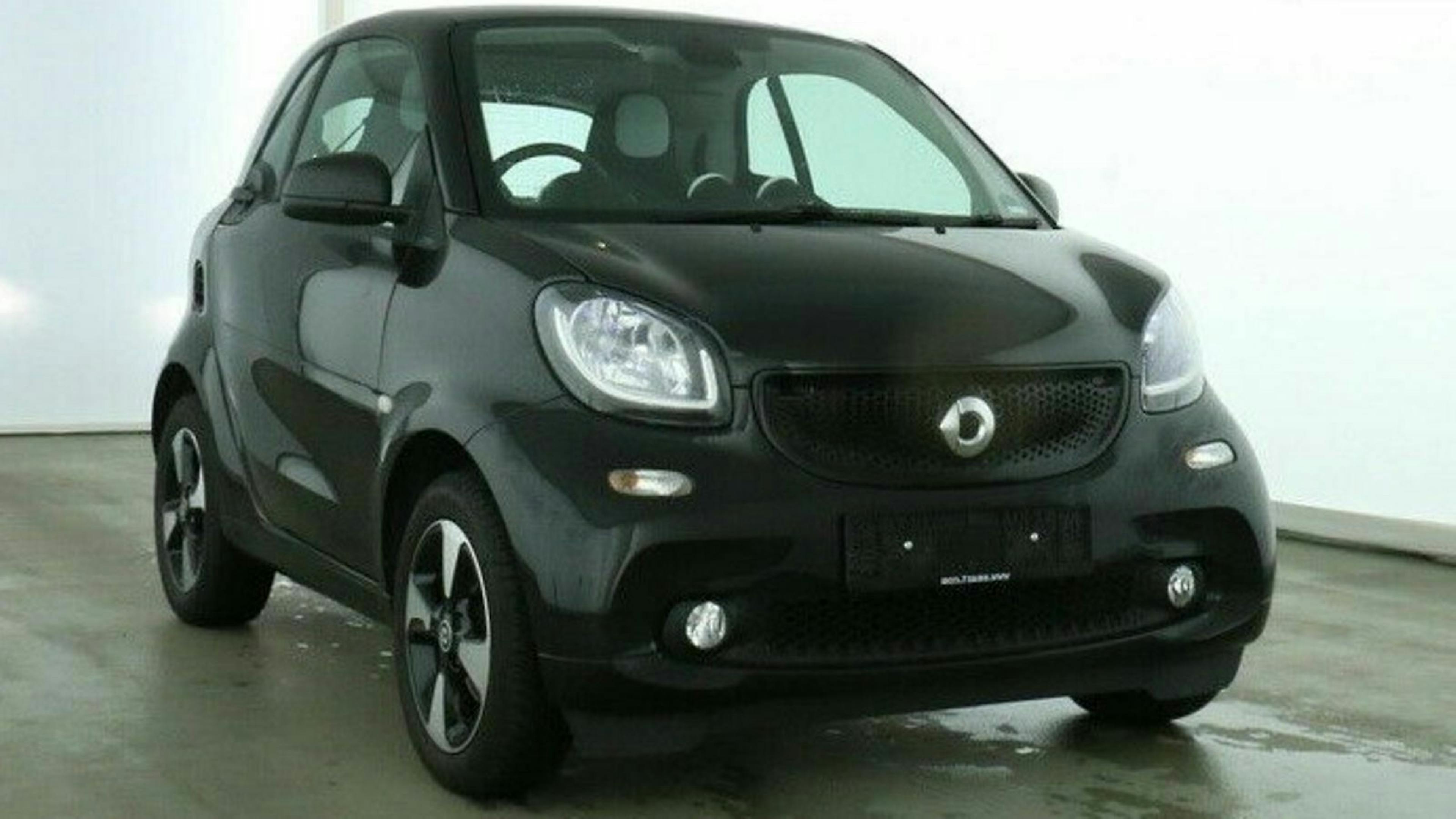 Schwarzes Smart Fortwo Auto in einem hellen Showroom, Vorderansicht. Leicht kompakte Bauweise mit zwei Türen und markanten Scheinwerfern.