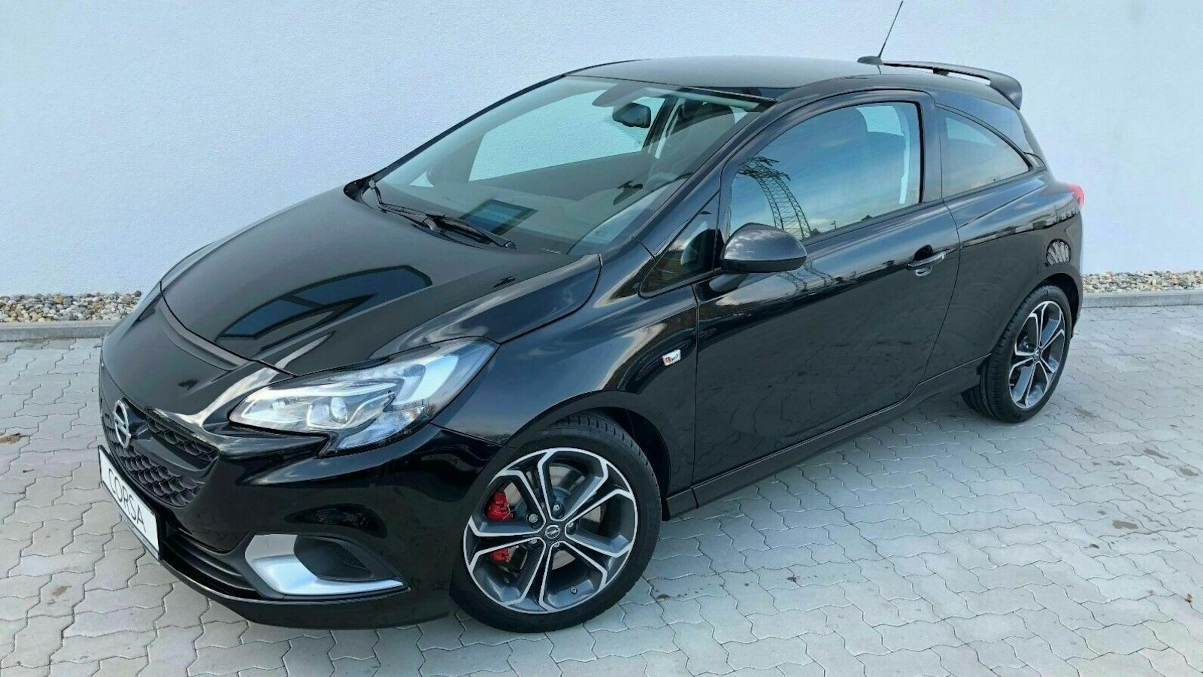 Schwarzer Opel Corsa, Dreitürer, auf Pflastersteinen geparkt, leicht von der Seite fotografiert.