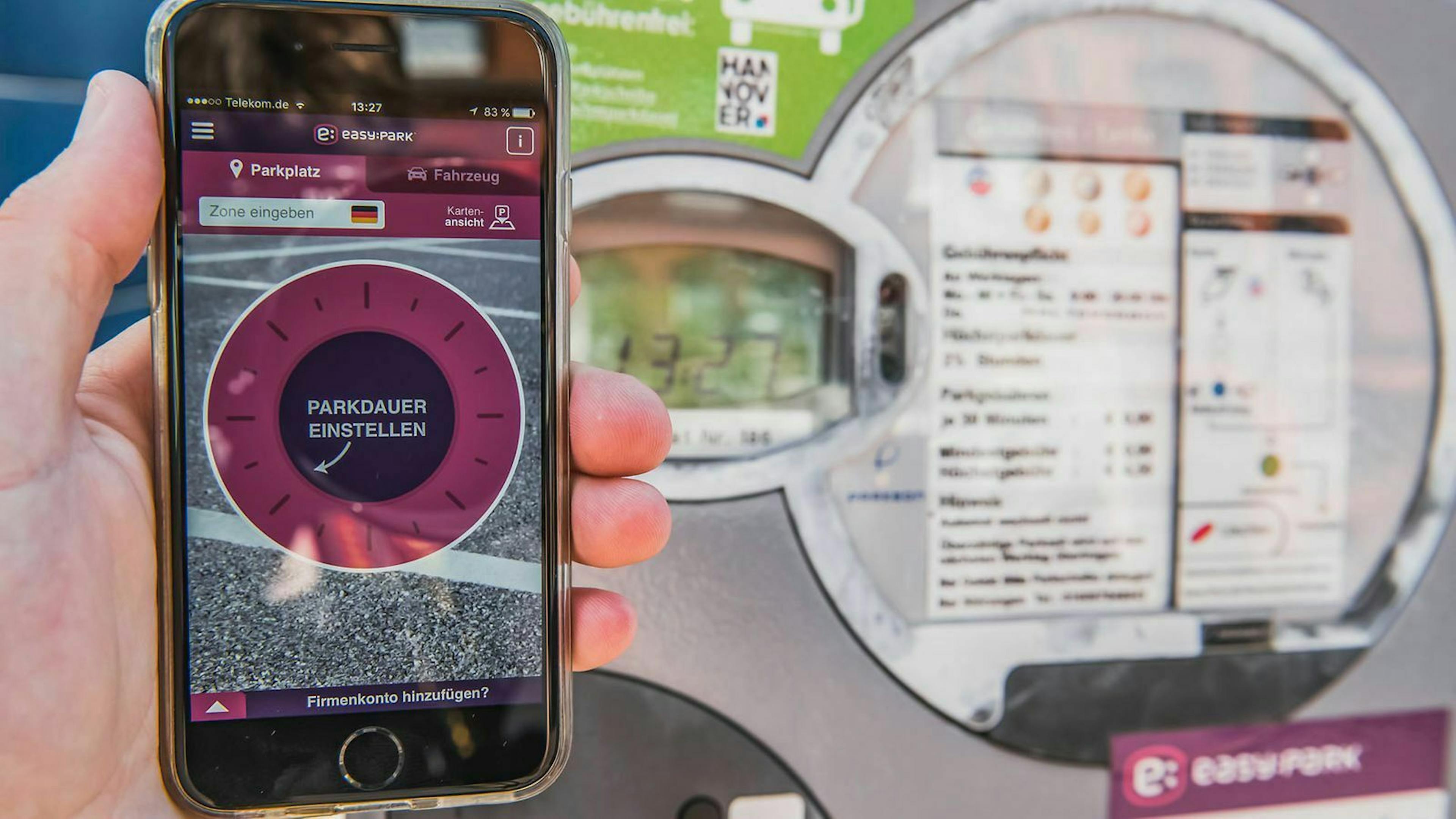 Jemand hält ein Smartphone, auf dem eine Park-App zur Abrechnung von Parkgebühren läuft. Im Hintergrund steht eine Parkuhr.
