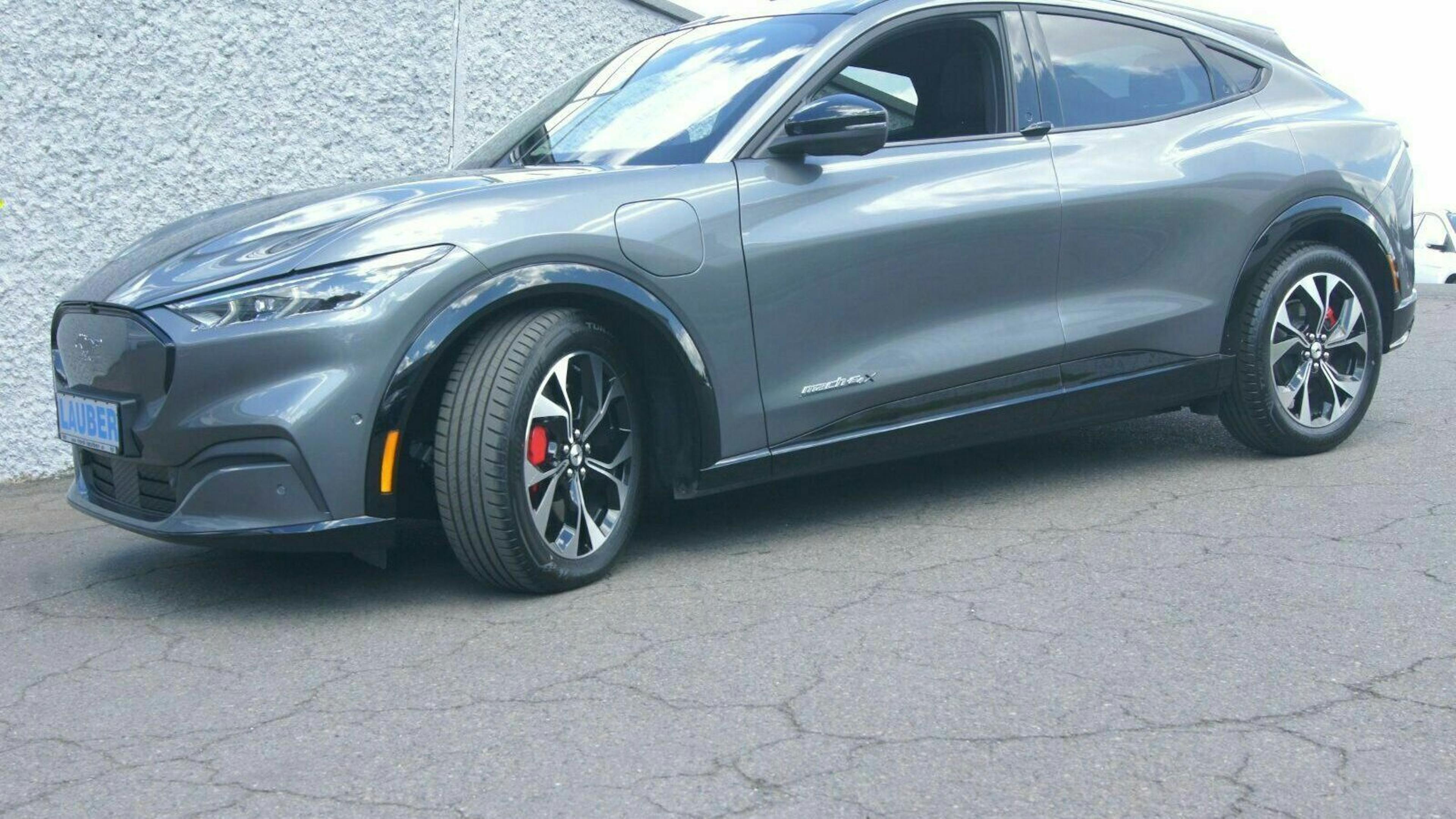 Ein grauer Mustang Mach E steht vor einem grauen Gebäude