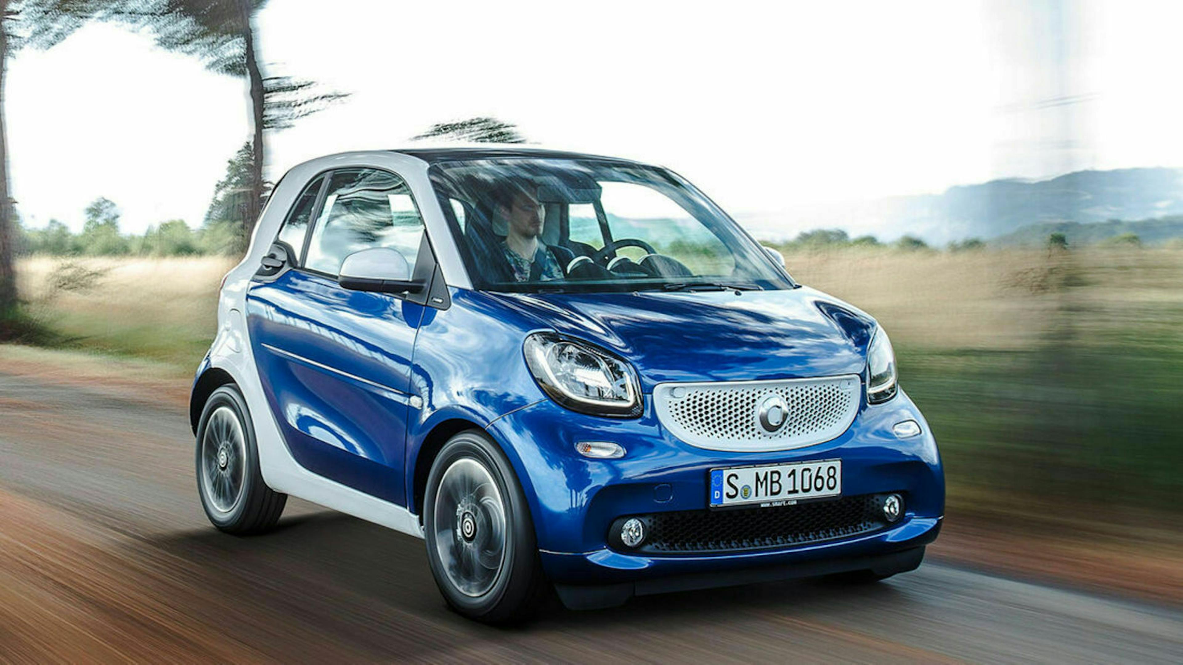 Ein blauer Smart Fortwo fährt eine Landstraße entlang.