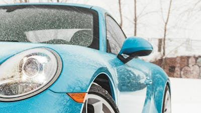 Ein blauer Pkw steht in einer verschneiten Landschaft.