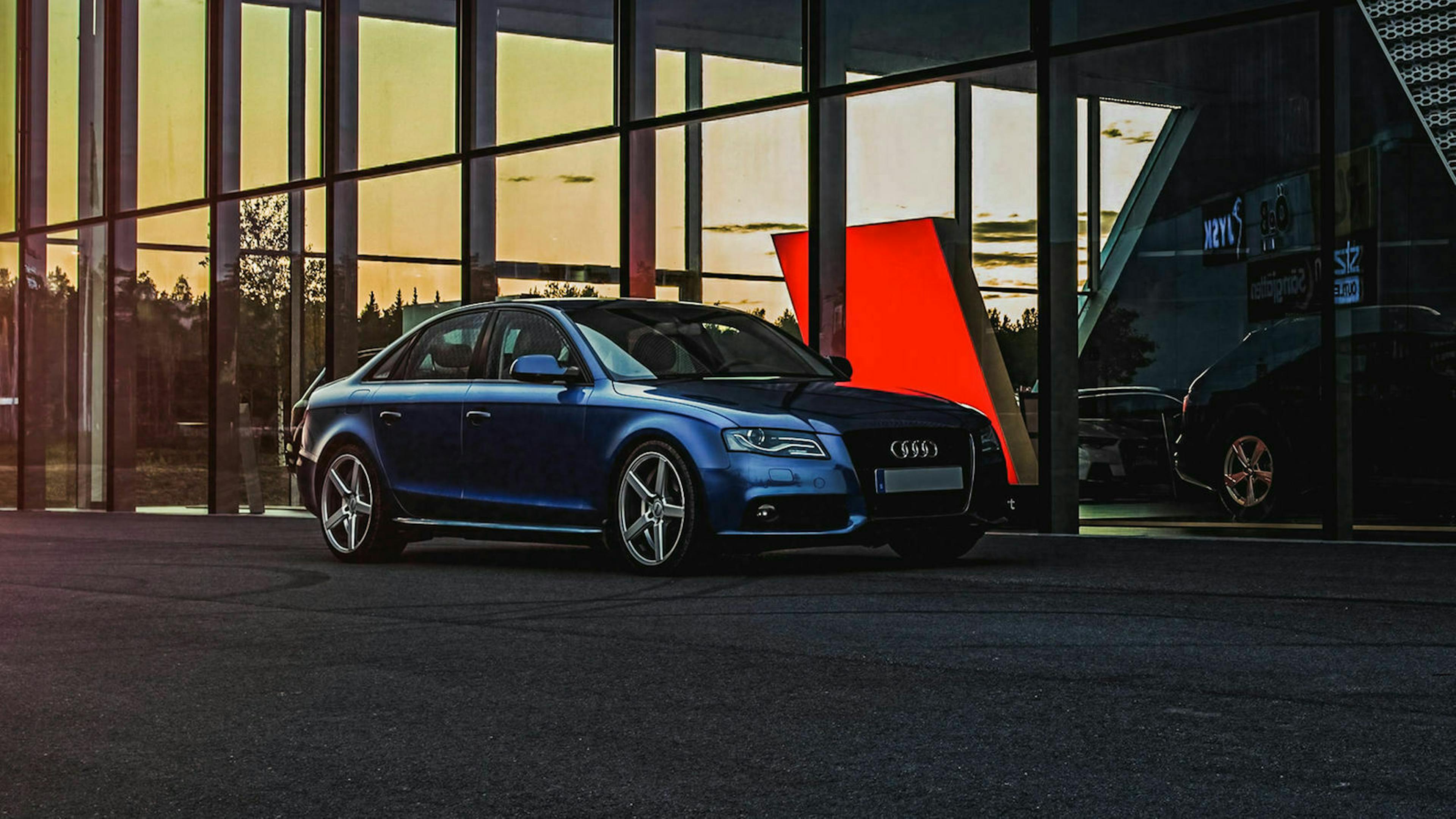 Ein gepflegter Gebrauchtwagen steht im Abendlicht vor der Fassade eines Autohändlers