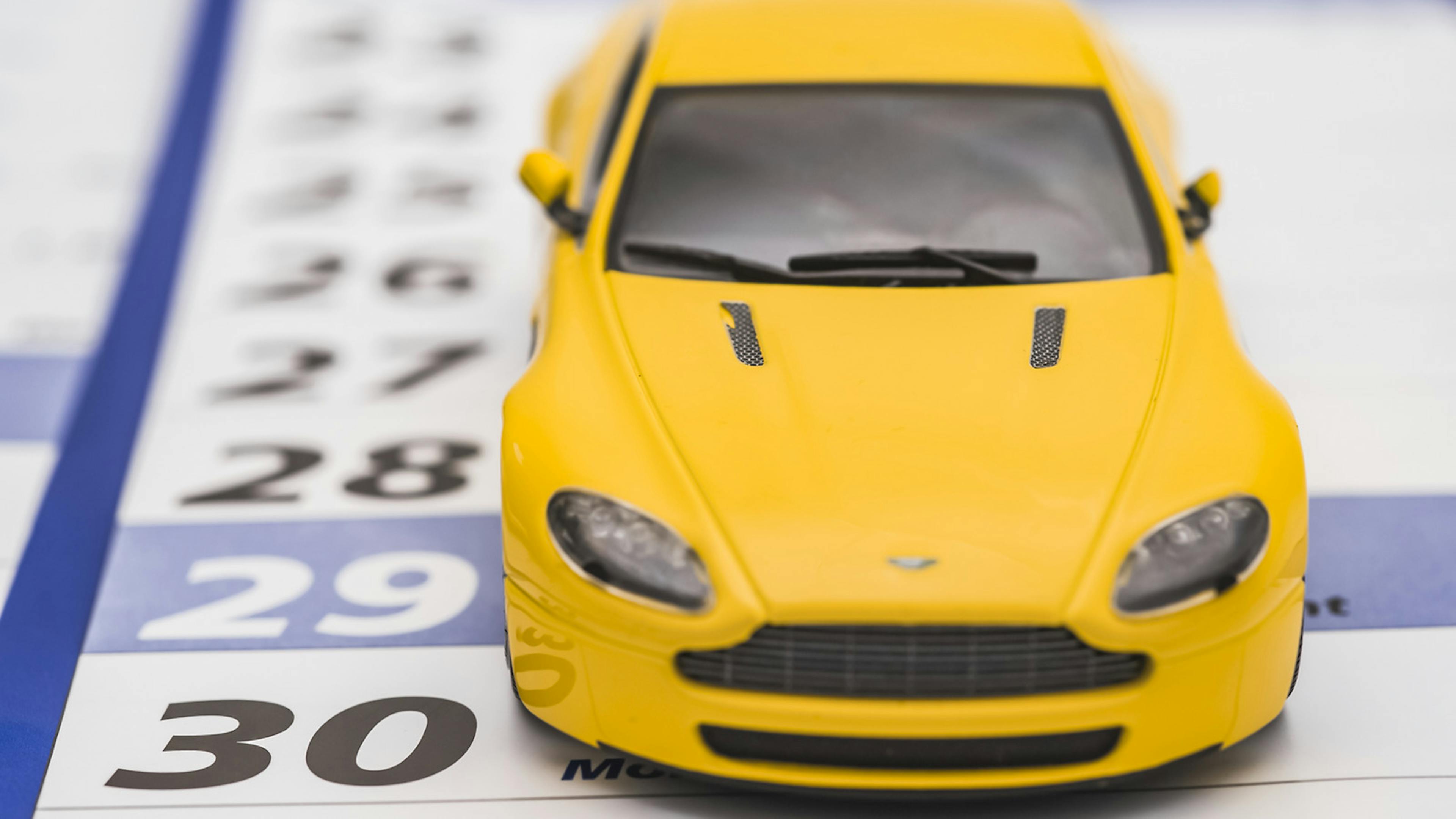 Ein gelbes Modell eines Sportwagens steht auf einem Kalenderblatt, mit dem Vorderreifen direkt neben der Zahl 29. 