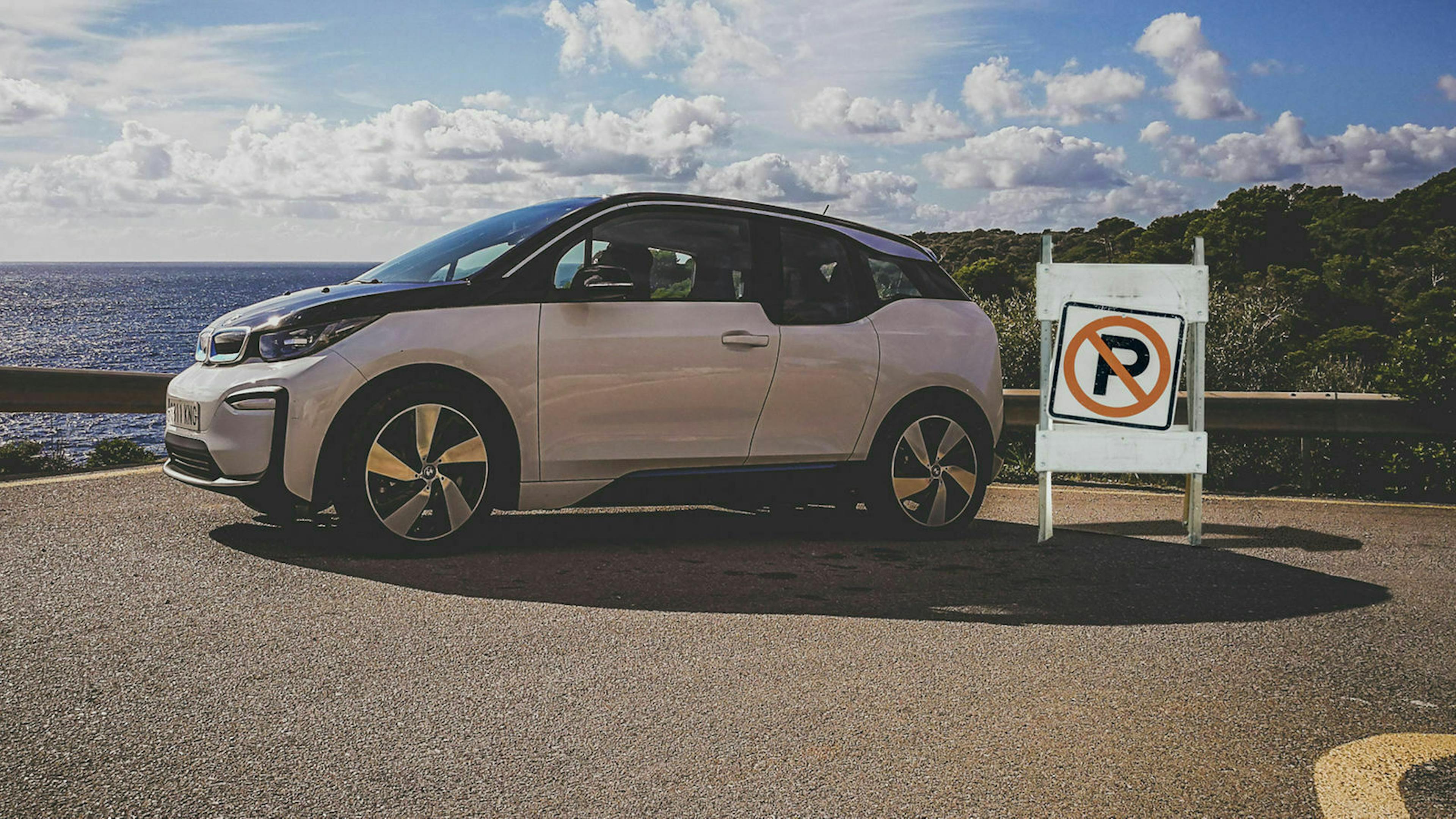 Das Bild zeigt ein Fahrzeug, das in einer Küstenstraße parkt. Daneben steht ein Parkverbots-Schild.